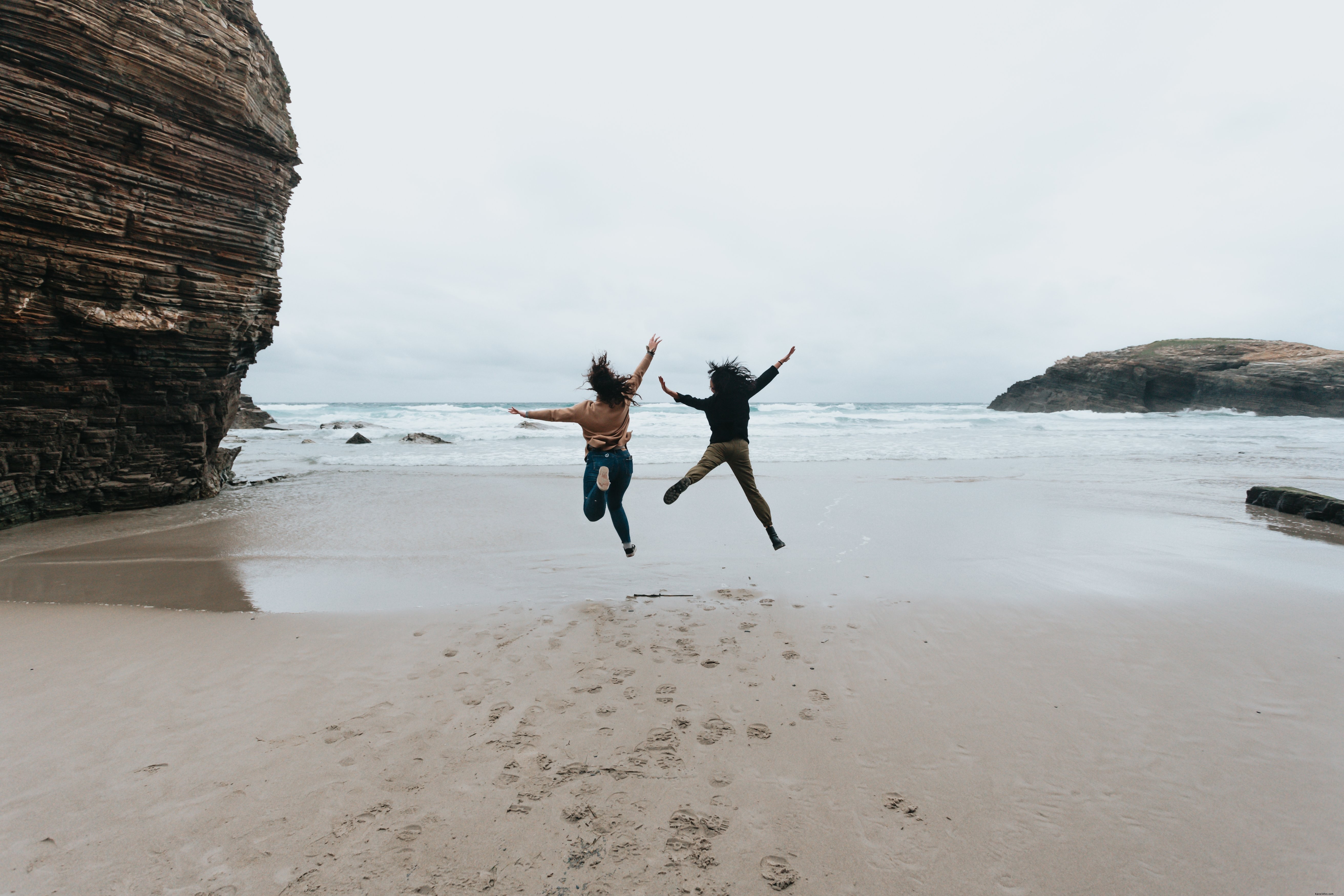 Duas pessoas pulam alto em uma foto de praia de areia 