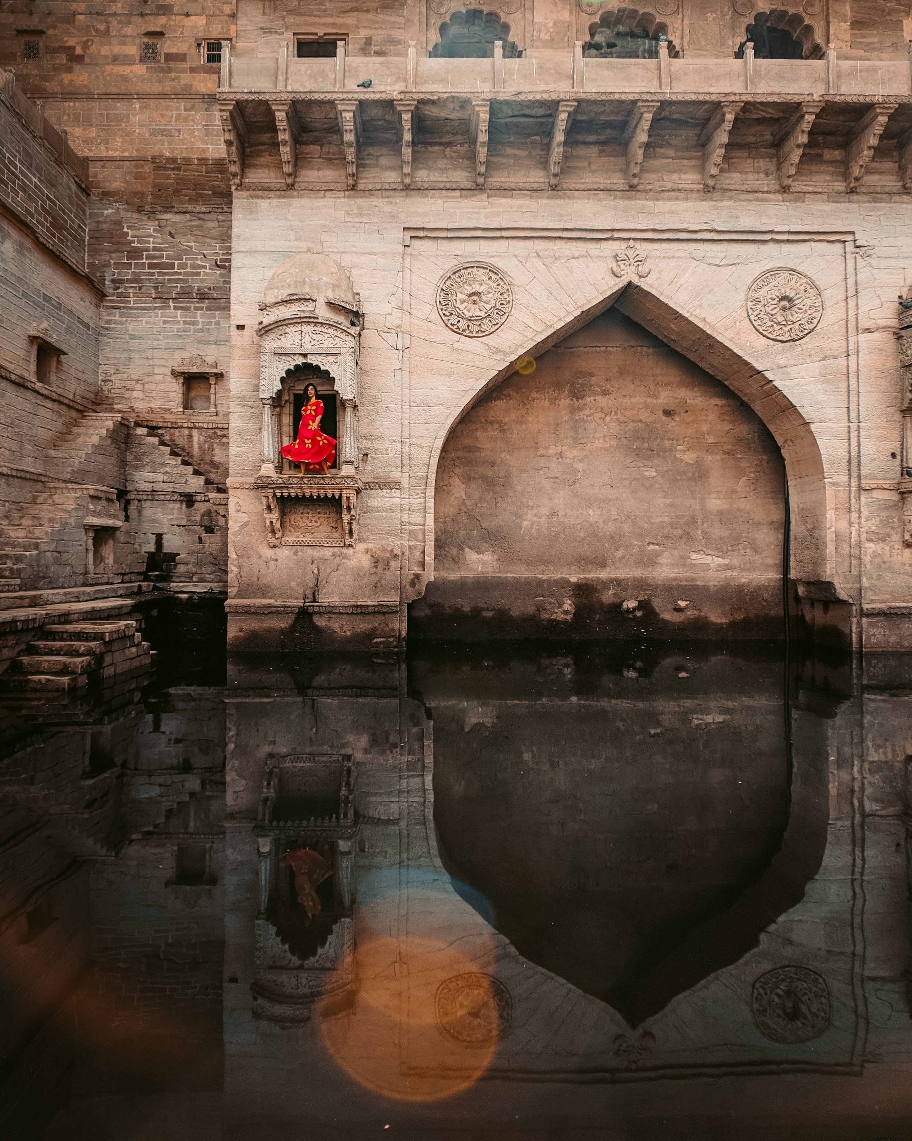 Mulher vestida de vermelho posa na frente de uma foto intrincada de um monumento 