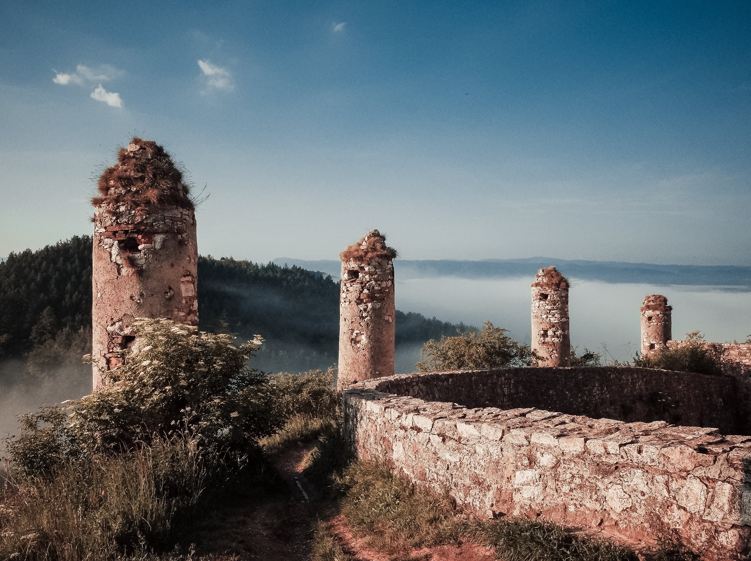 Foto de ruinas cubiertas de hierba con vistas a las cimas de las montañas 