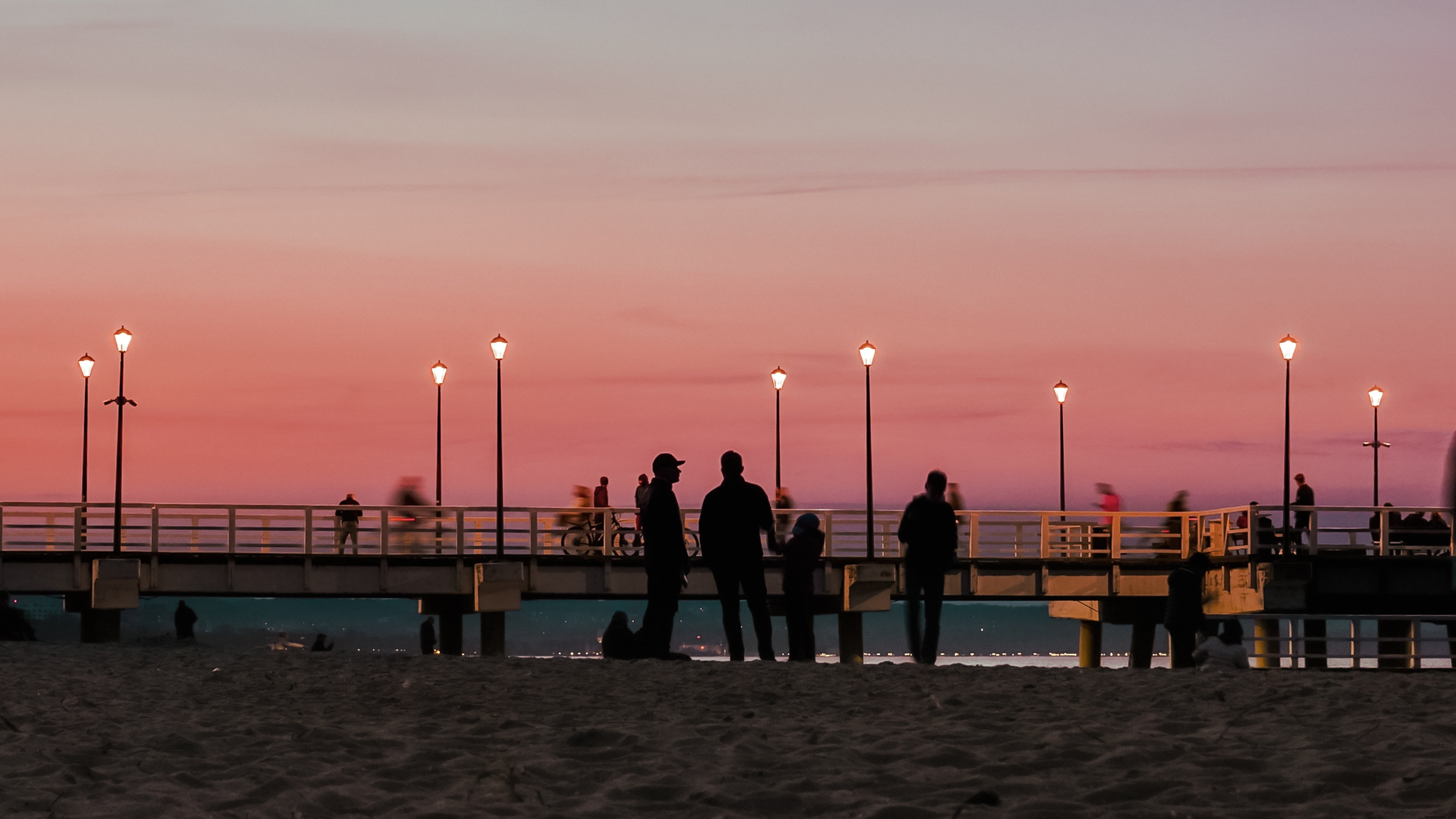 Les gens se tiennent sur la plage par une jetée au coucher du soleil Photo 