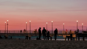 Les gens se tiennent sur la plage par une jetée au coucher du soleil Photo 