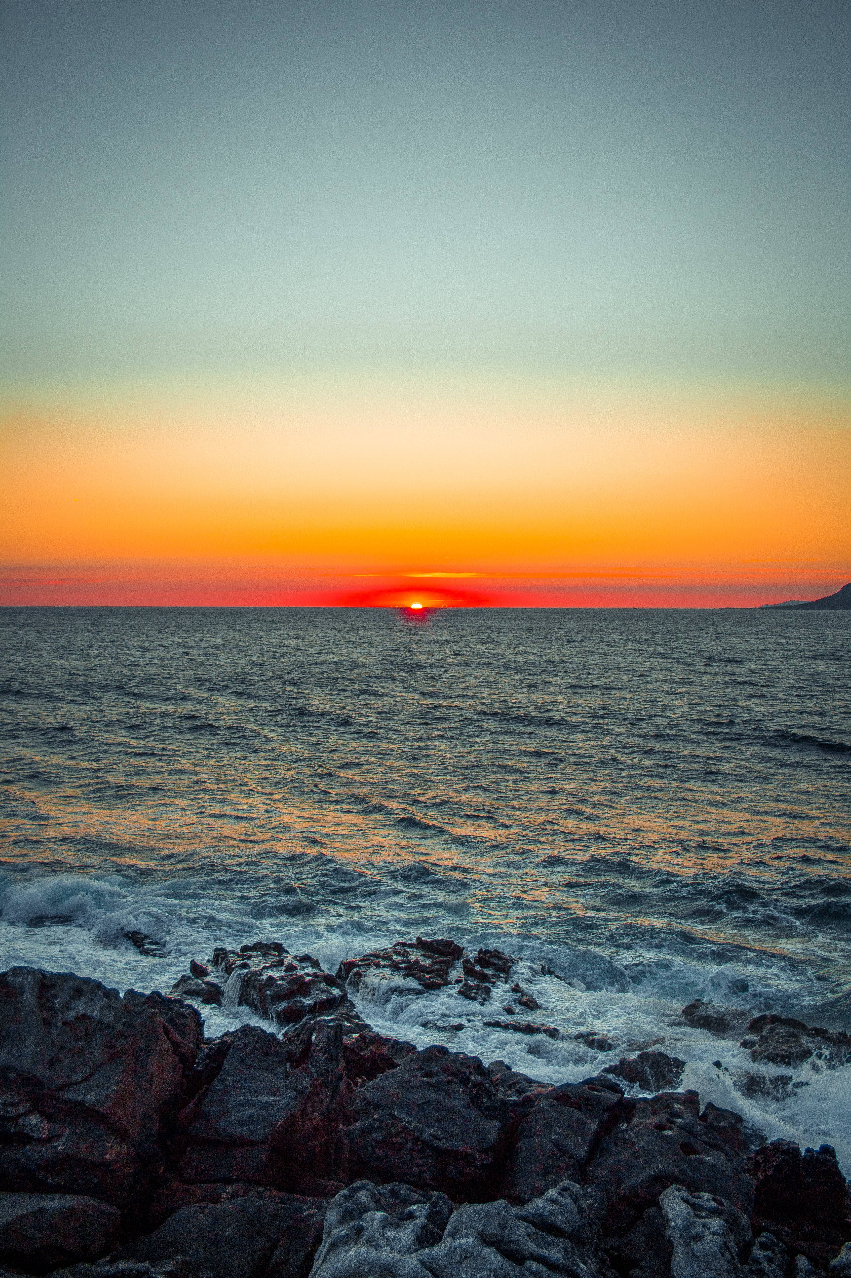 磯に沈む夕日の最後の瞬間写真 