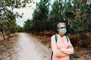 フェイスマスクの女性がハイキングトレイルの写真の上に立つ 