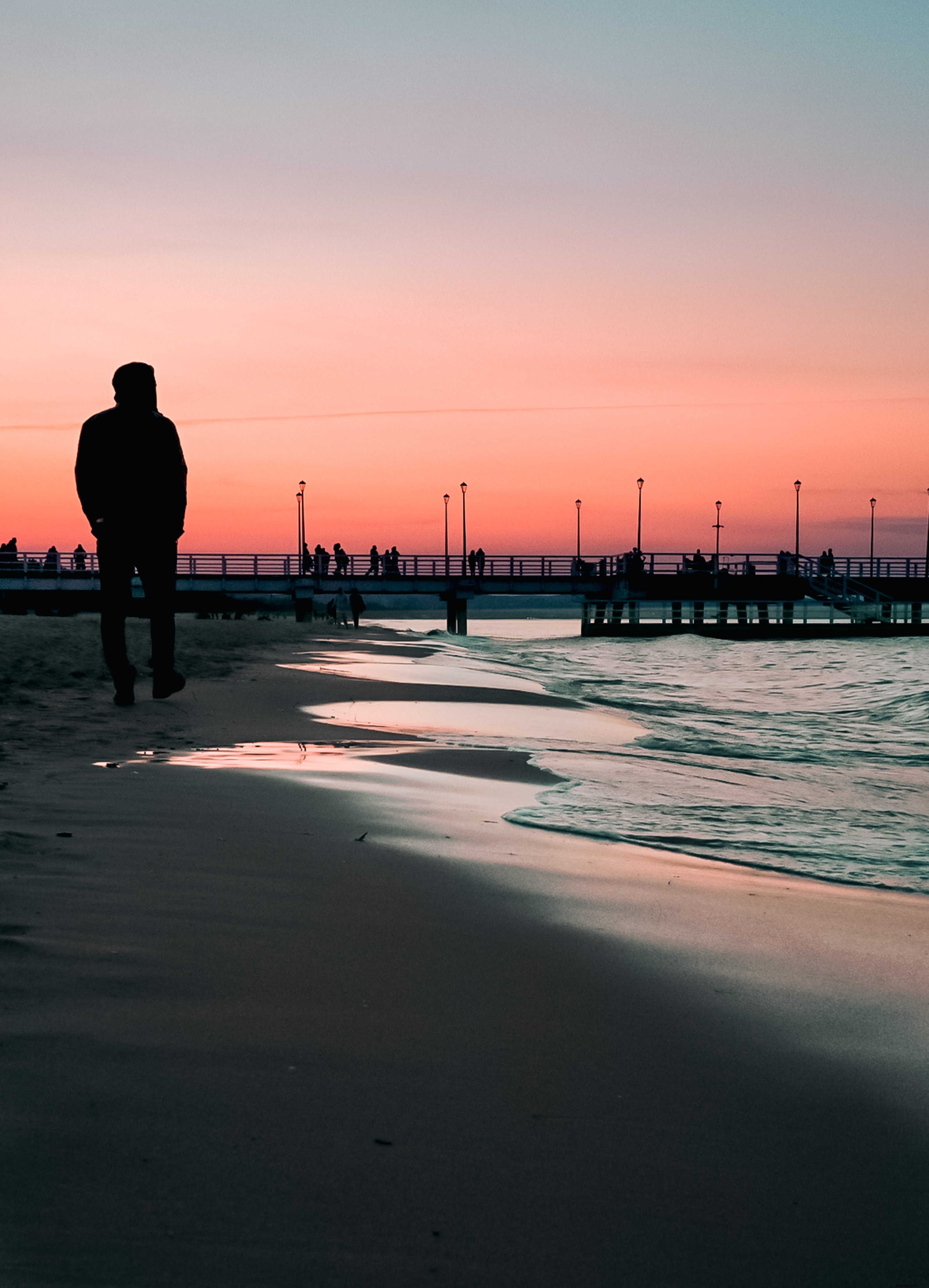 Paseo por la playa al atardecer con un muelle en la distancia Foto 