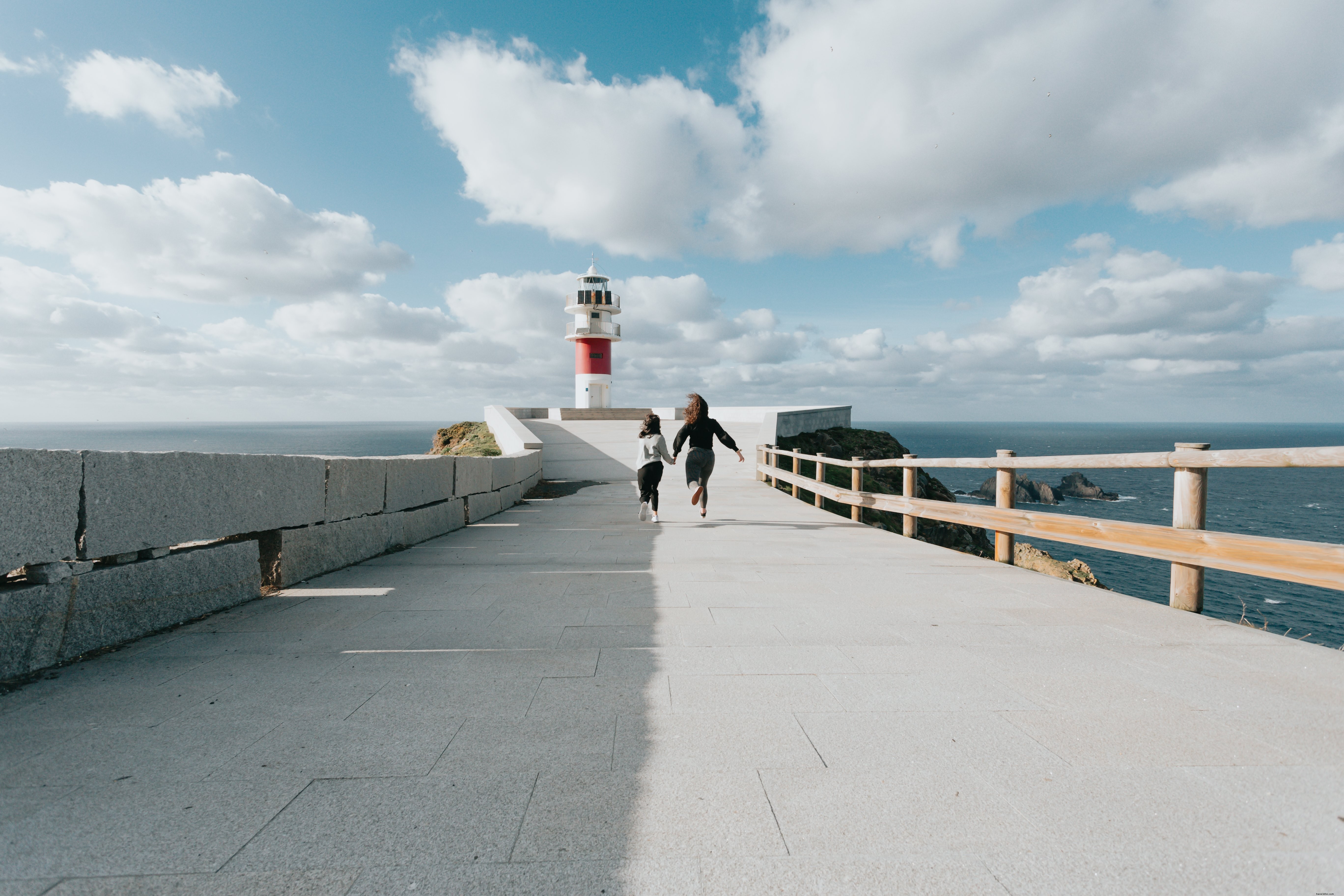 Dos personas corren por una carretera pavimentada hacia un faro Foto 