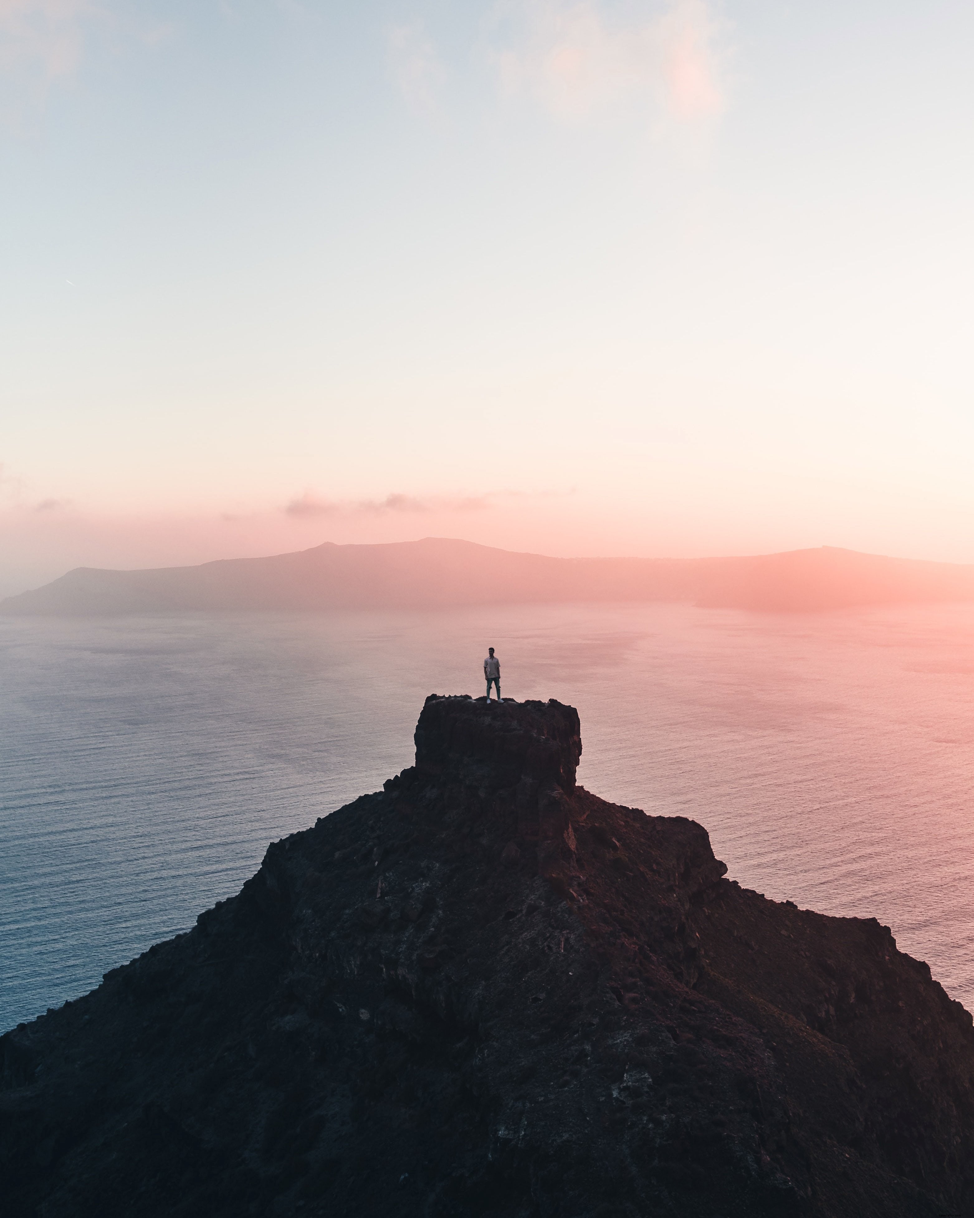 夕日の写真を撮って遠くの崖の上に立っている人 