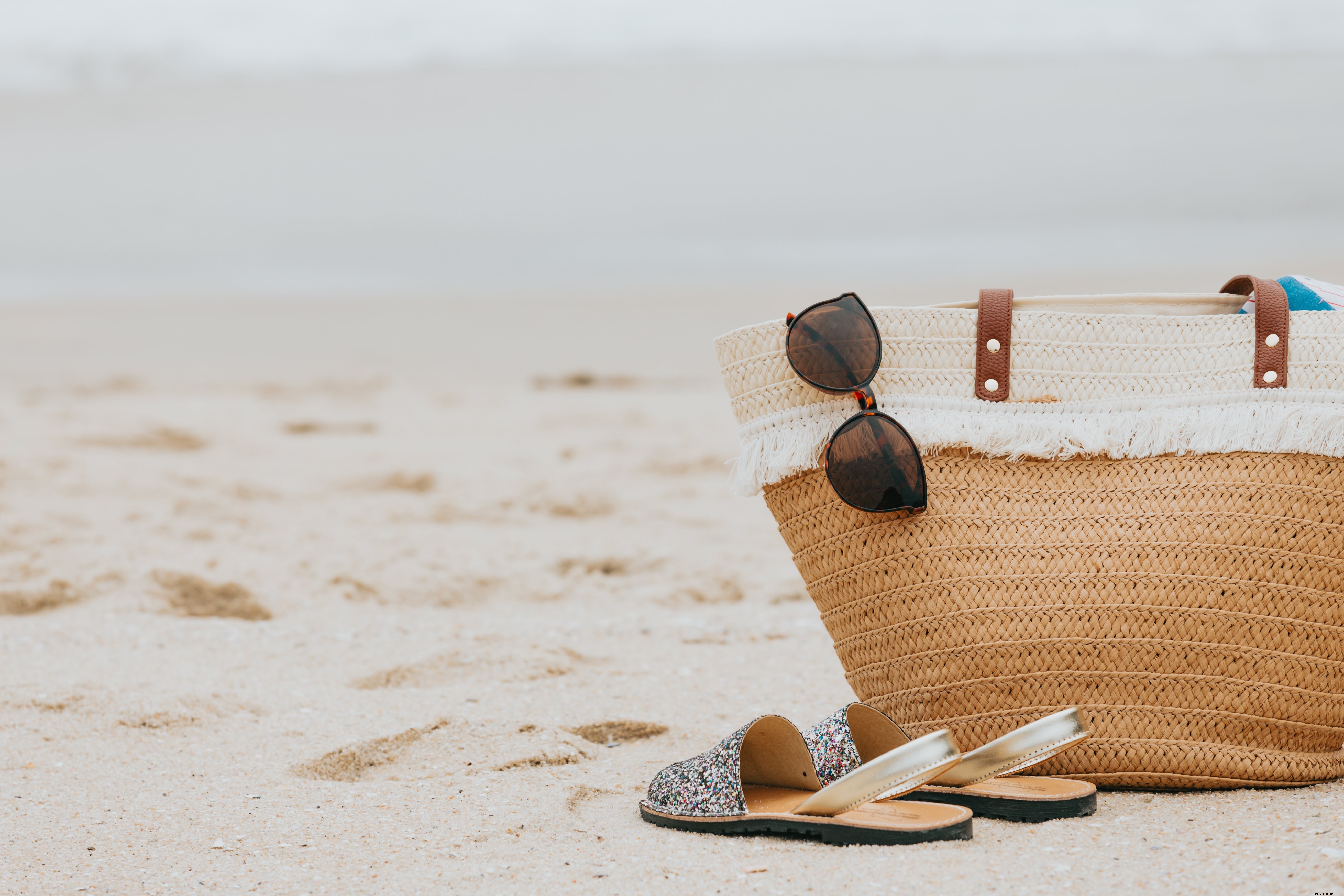 Praia de areia com sandálias de óculos de sol e uma foto de bolsa de praia 