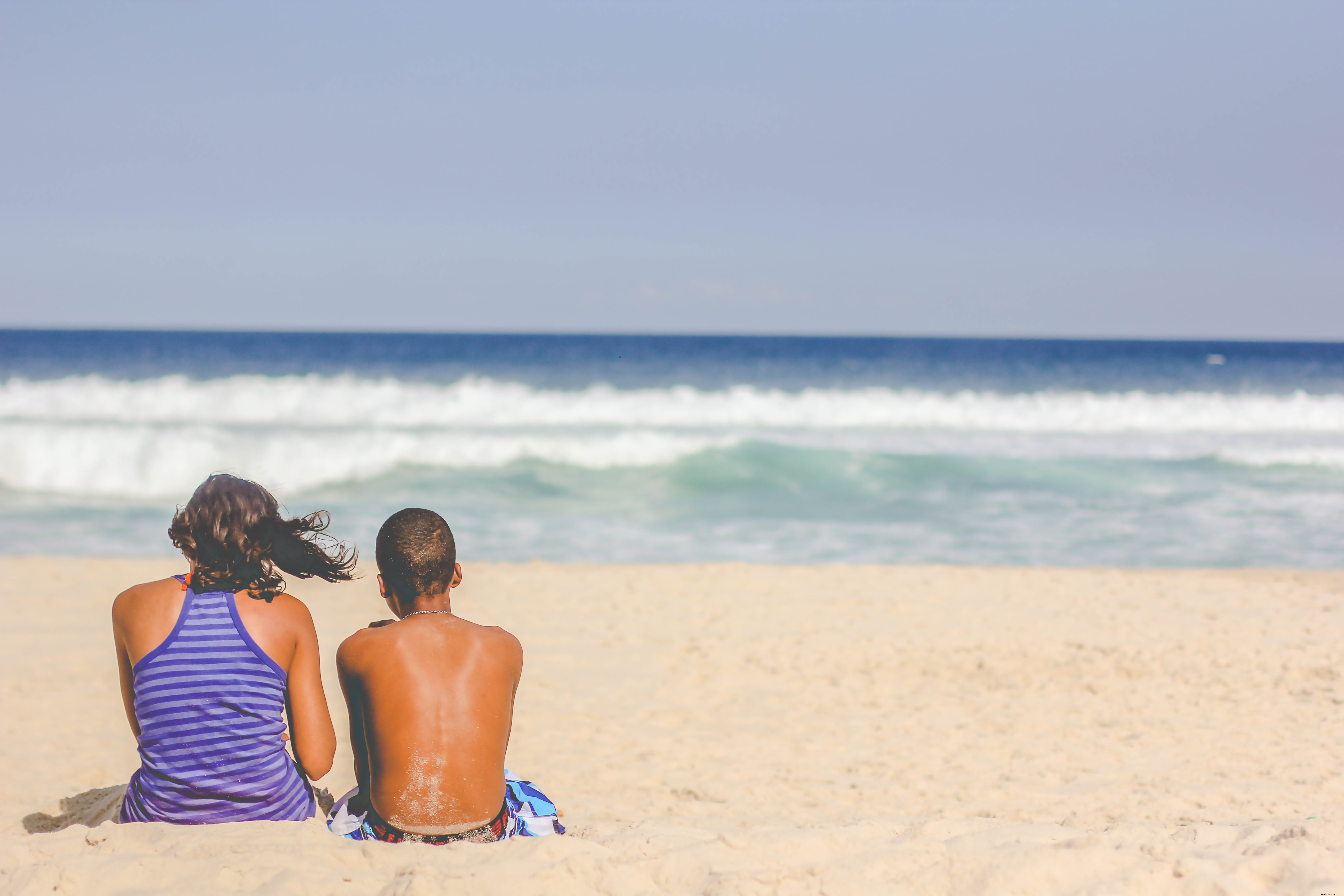 As pessoas se sentam na praia e olham para o oceano. 