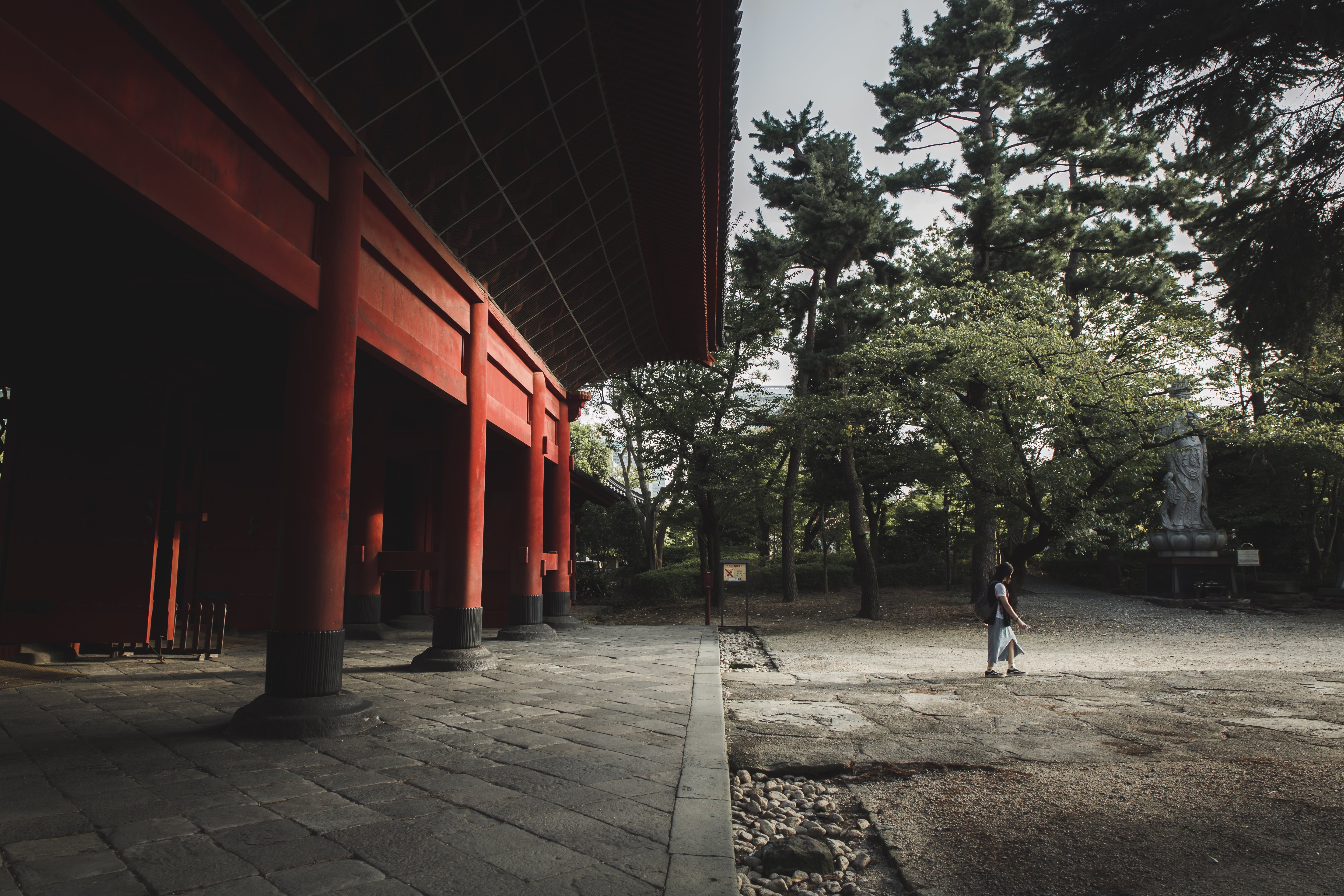 写真を歩いている人と赤い建物と木々 