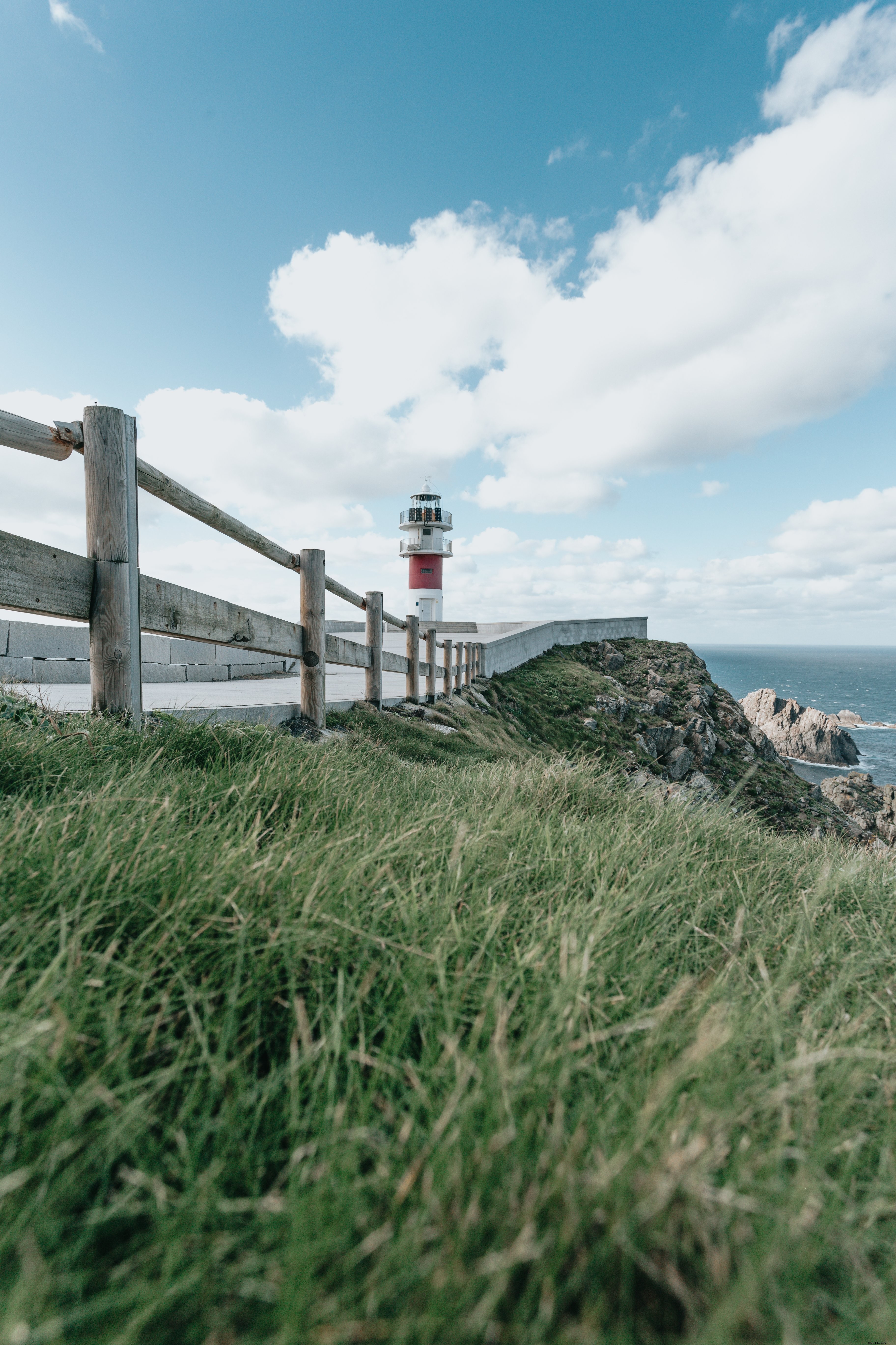 Grama verde e uma cerca de madeira com um farol atrás dela. Foto 