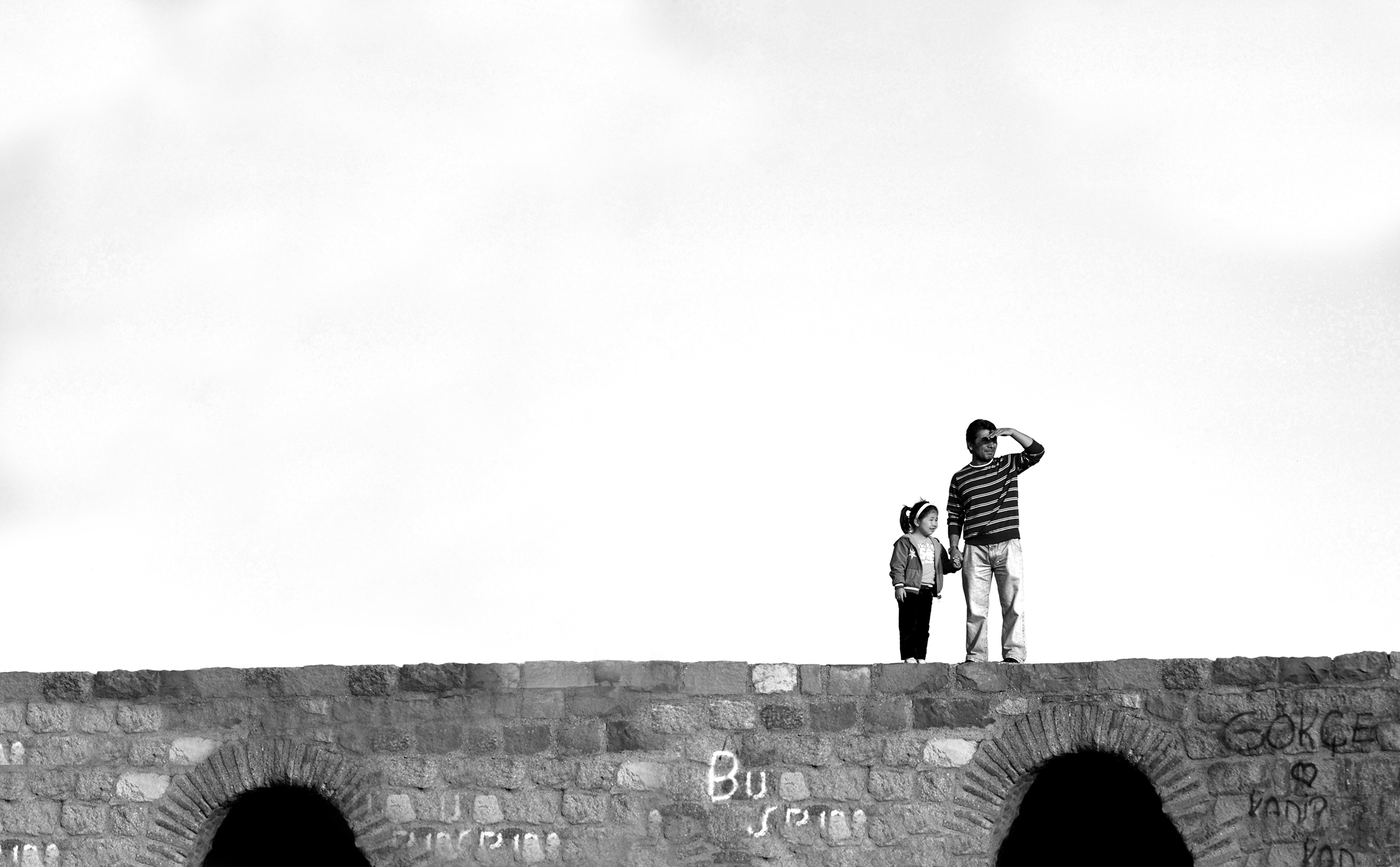 Duas pessoas em pé sobre uma ponte de pedra em preto e branco. 