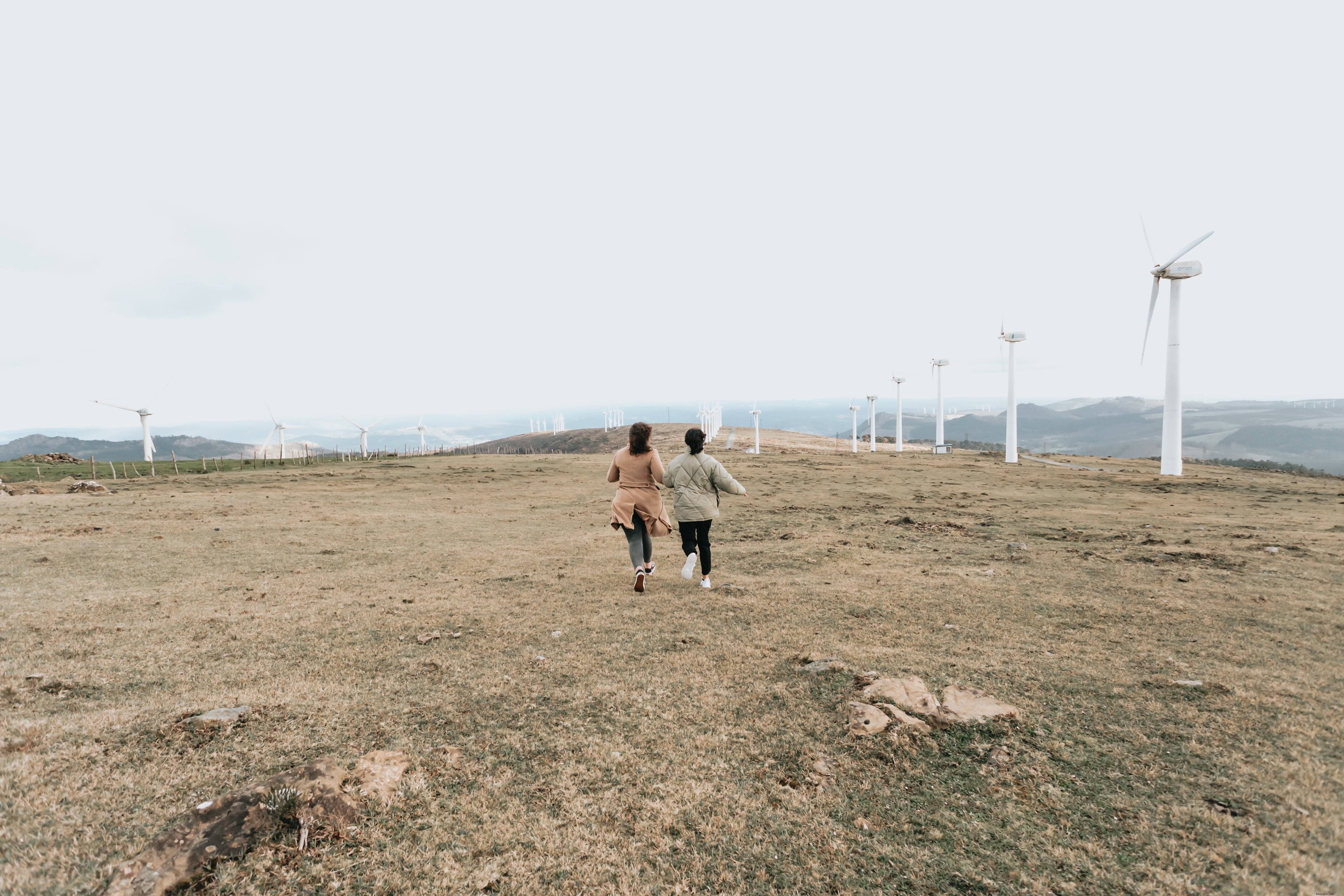 Duas pessoas caminham entre altos moinhos de vento branco 