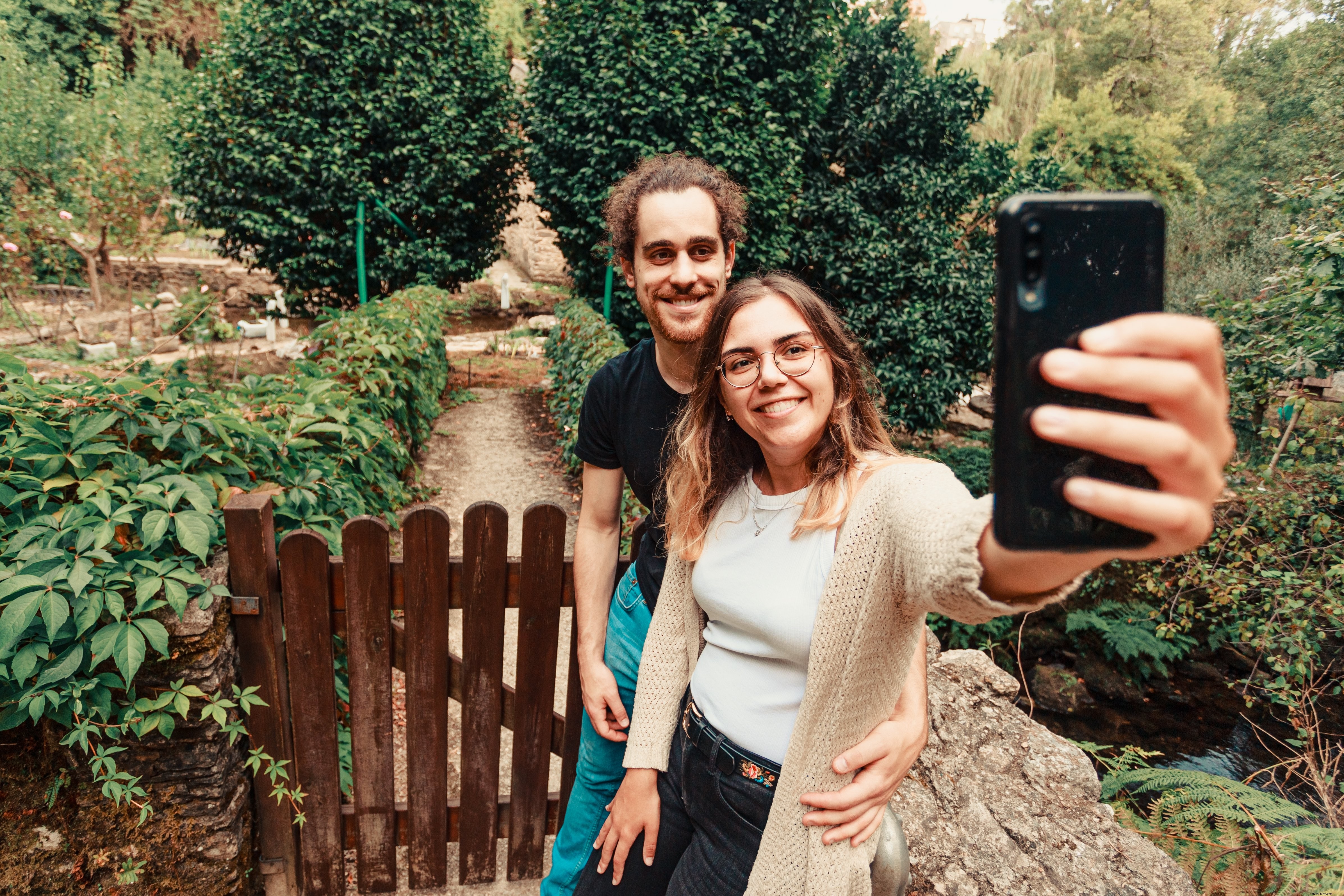 Casal sorrindo para um telefone celular em pé ao ar livre. 