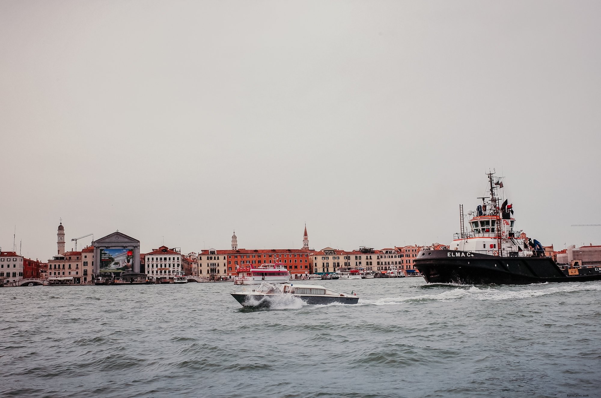 Barcos em águas onduladas com a costa forrada de edifícios. 