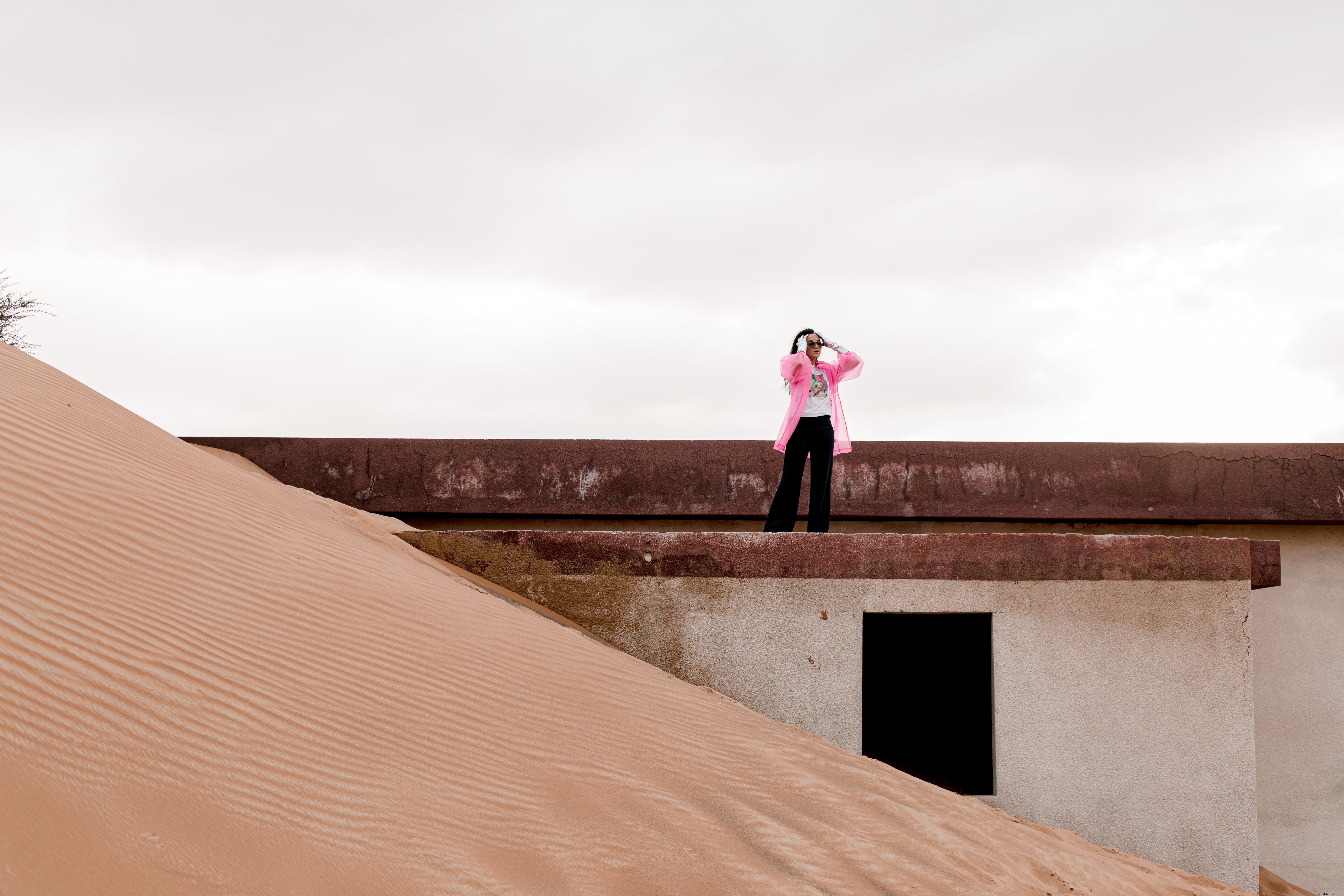 Foto de um prédio coberto de areia por uma pessoa com um casaco rosa 