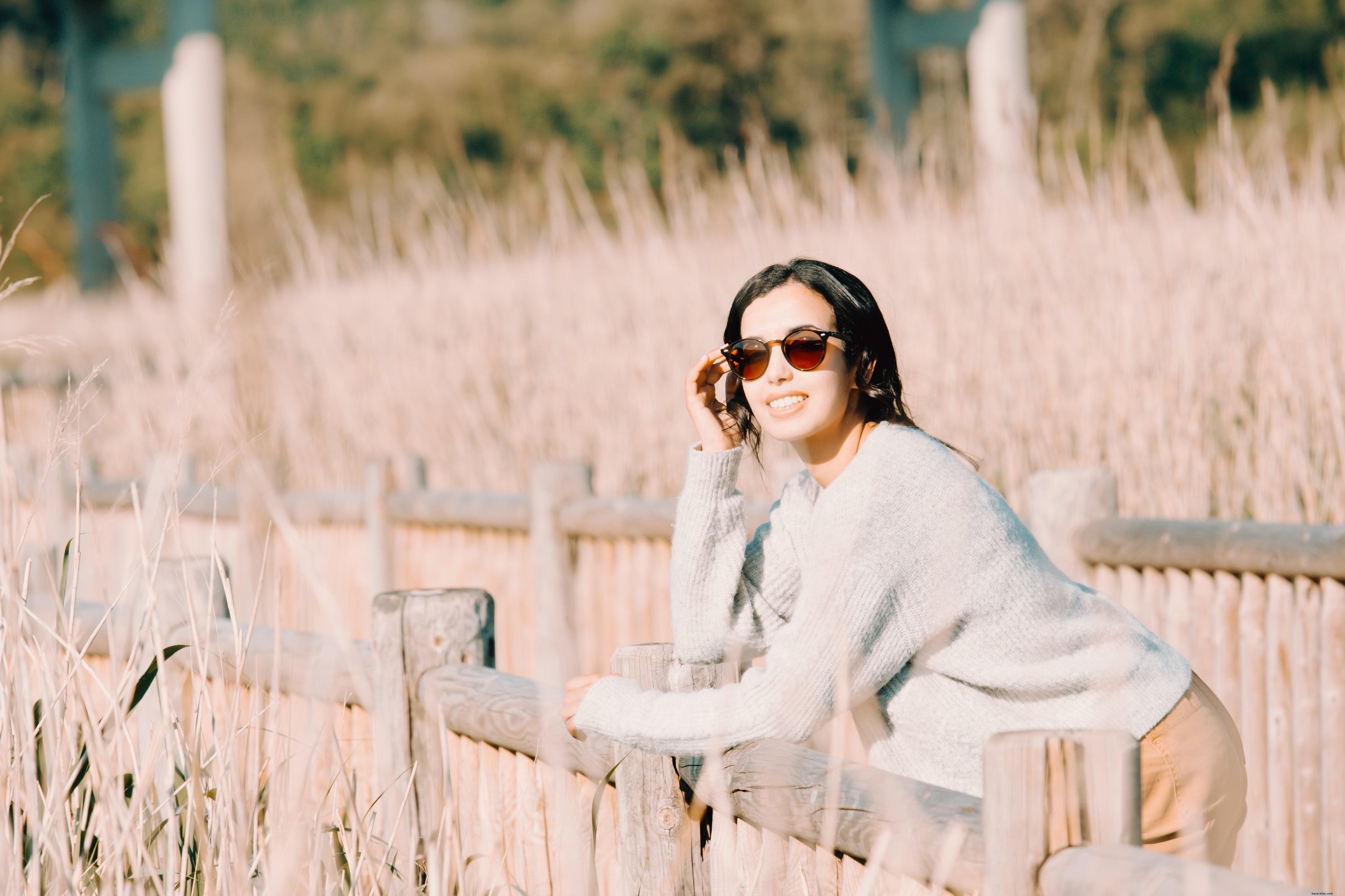 La donna con gli occhiali da sole si appoggia a una staccionata di legno Foto 