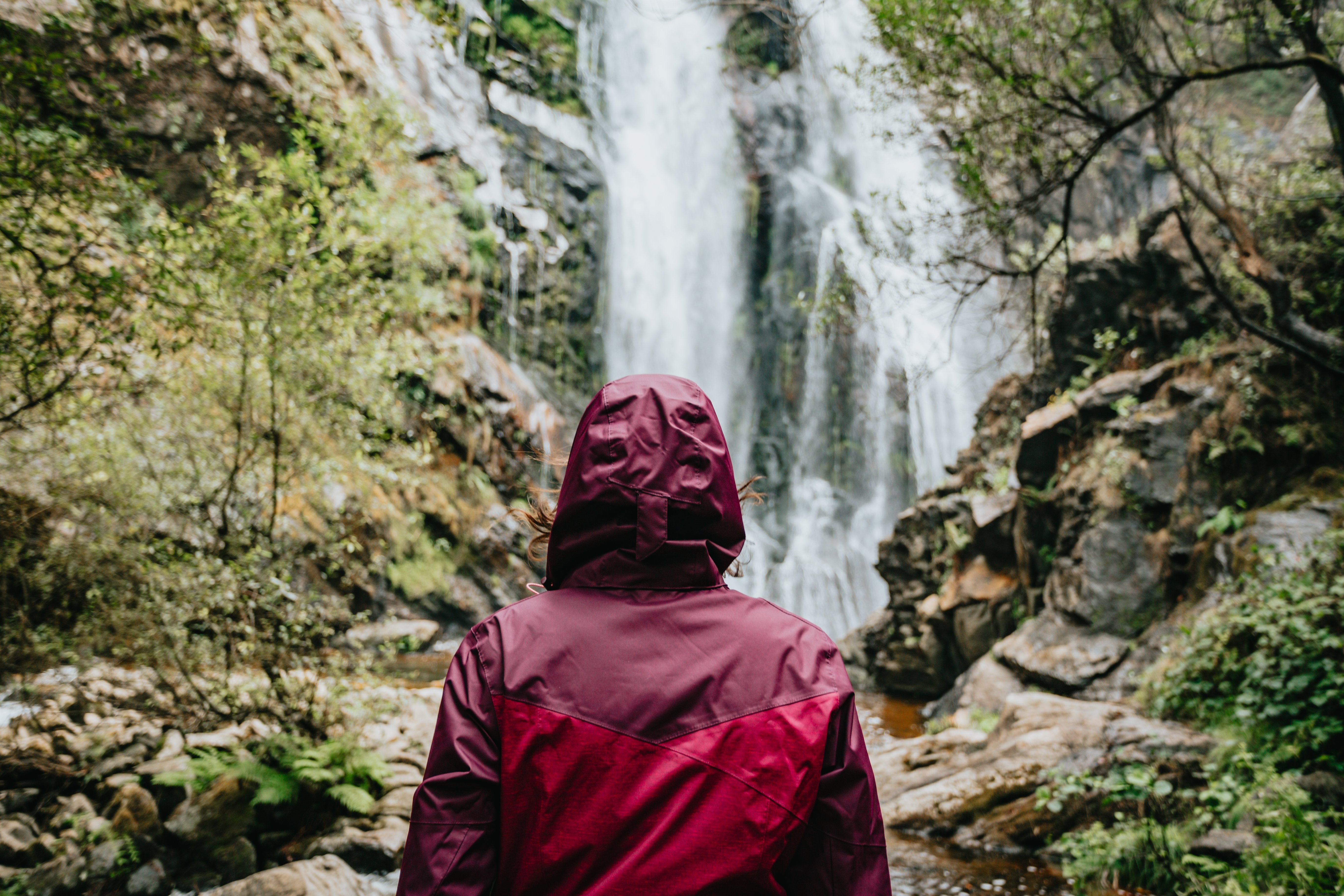 Pessoa vestindo uma capa de chuva olha para a foto de uma cachoeira alta 