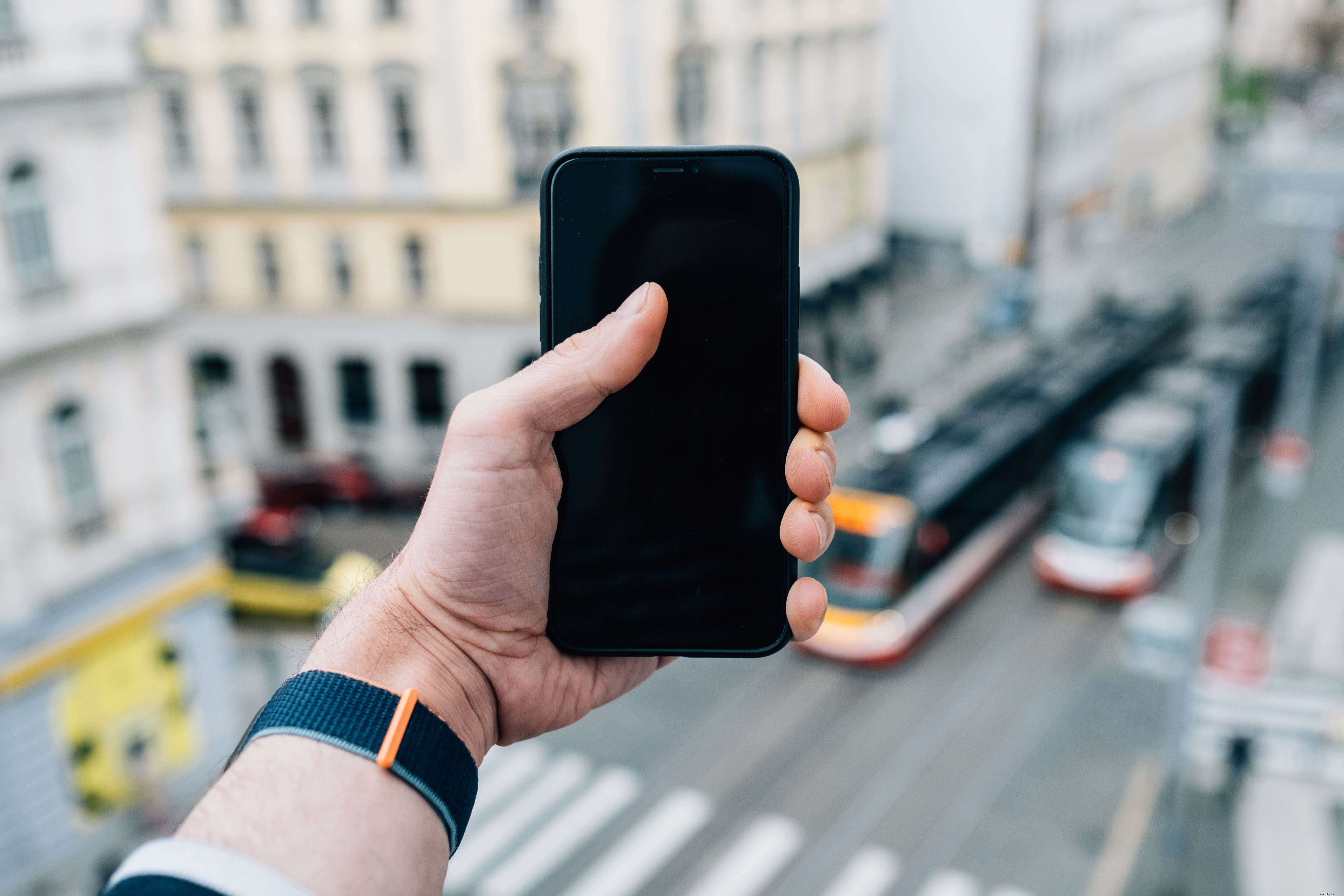 Mão segura um celular preto com uma foto fora de foco 