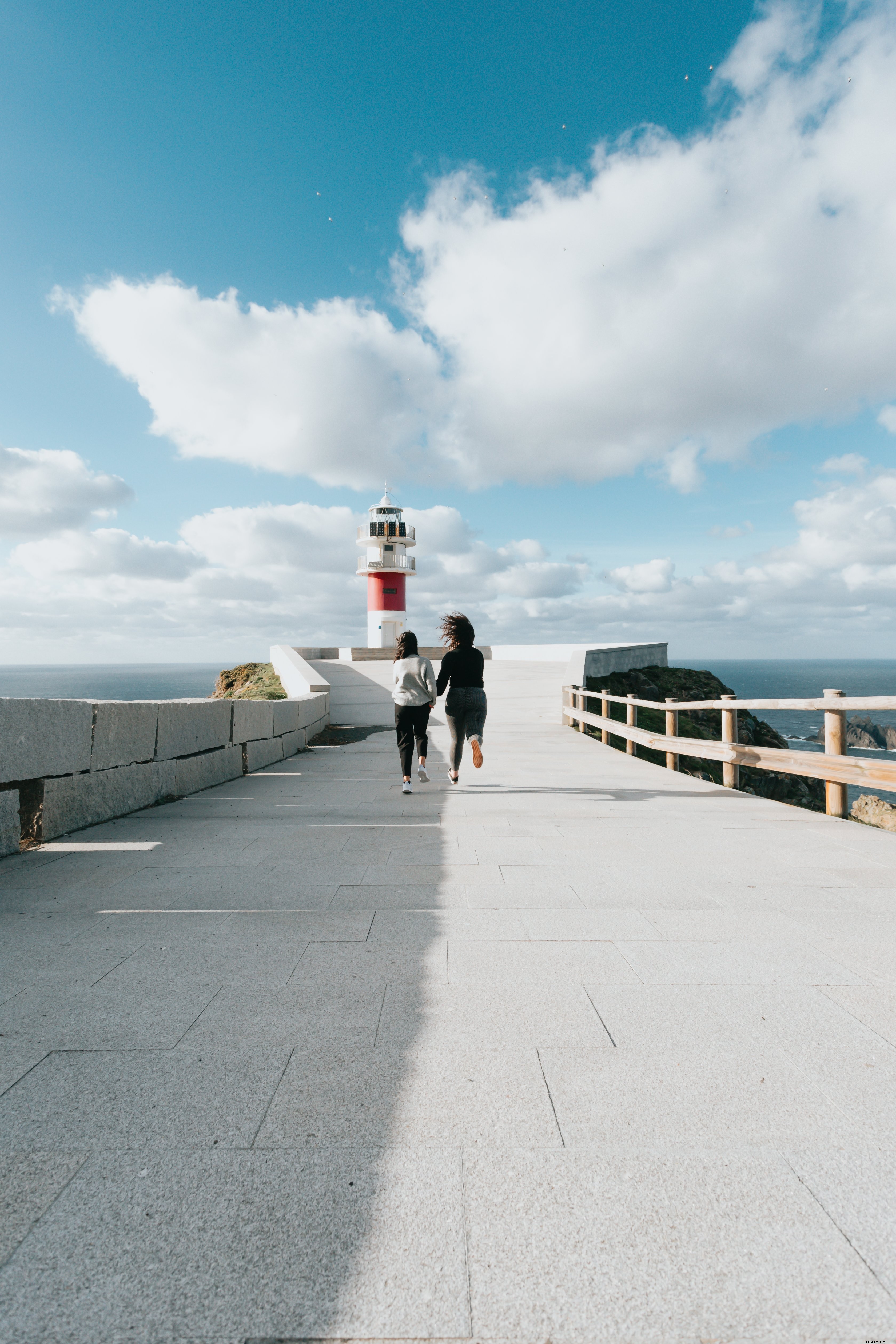 Duas pessoas correm em direção a um farol vermelho e branco. 