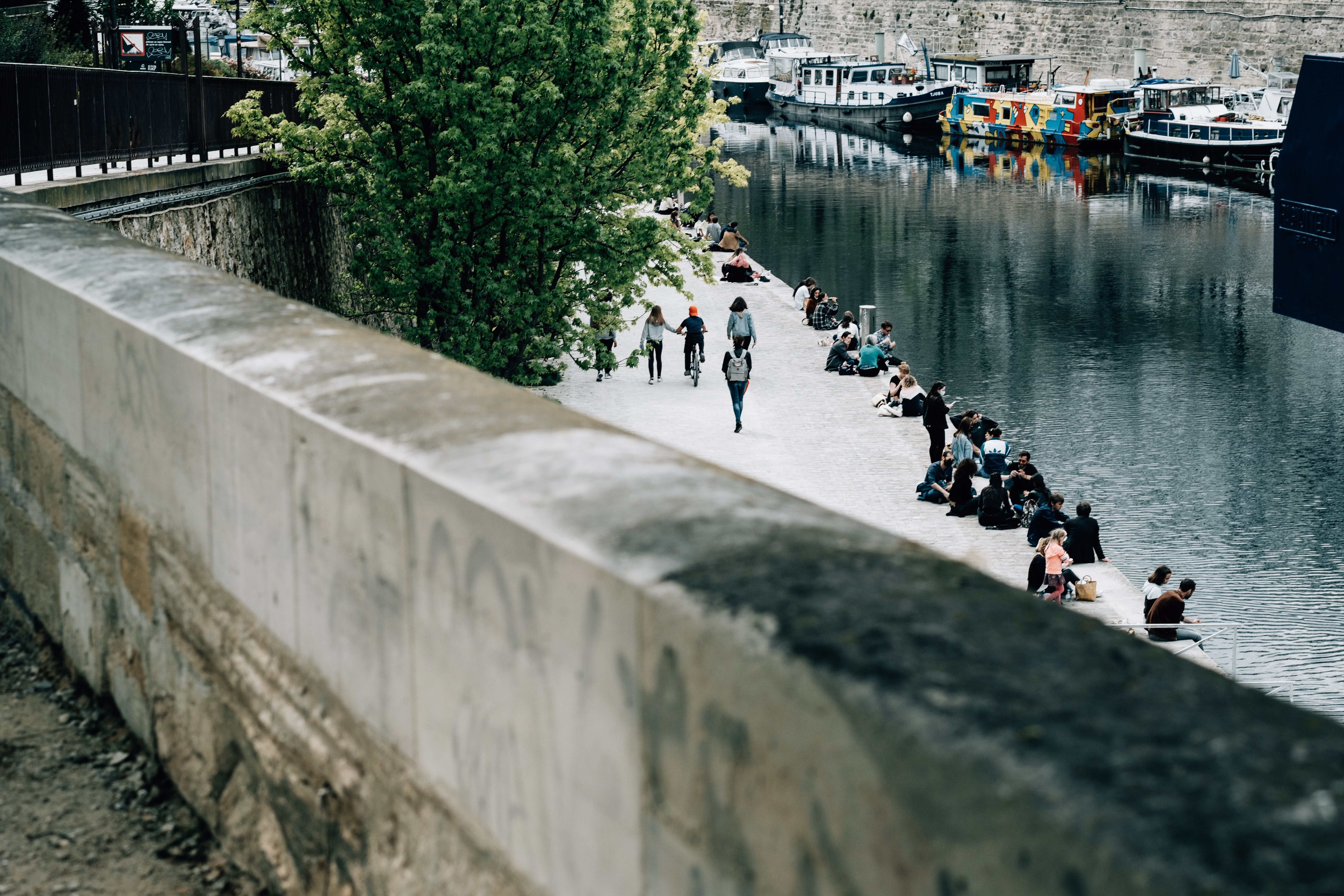 Canal com pessoas sentadas e barcos enfileirados na lateral. Foto 