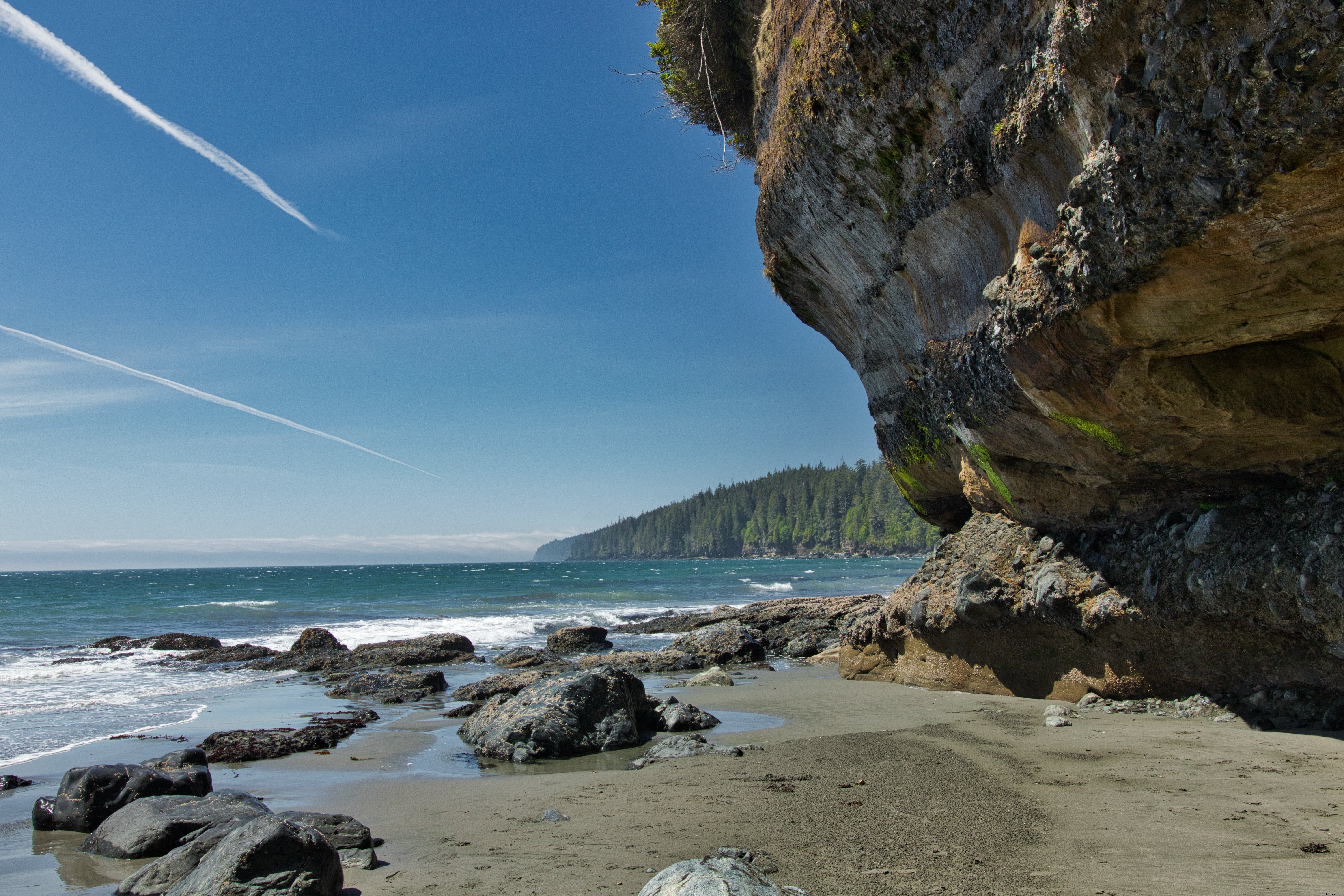 岩の崖が青い水の隣の砂浜にぶら下がっている写真 