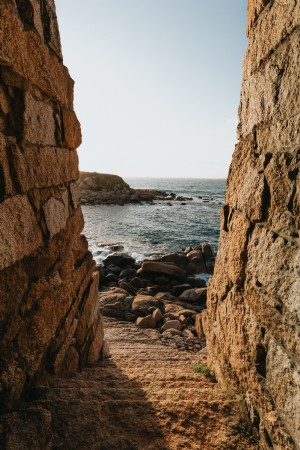 Escadas de pedra levam a uma costa coberta de pedras com fotos de ondas 