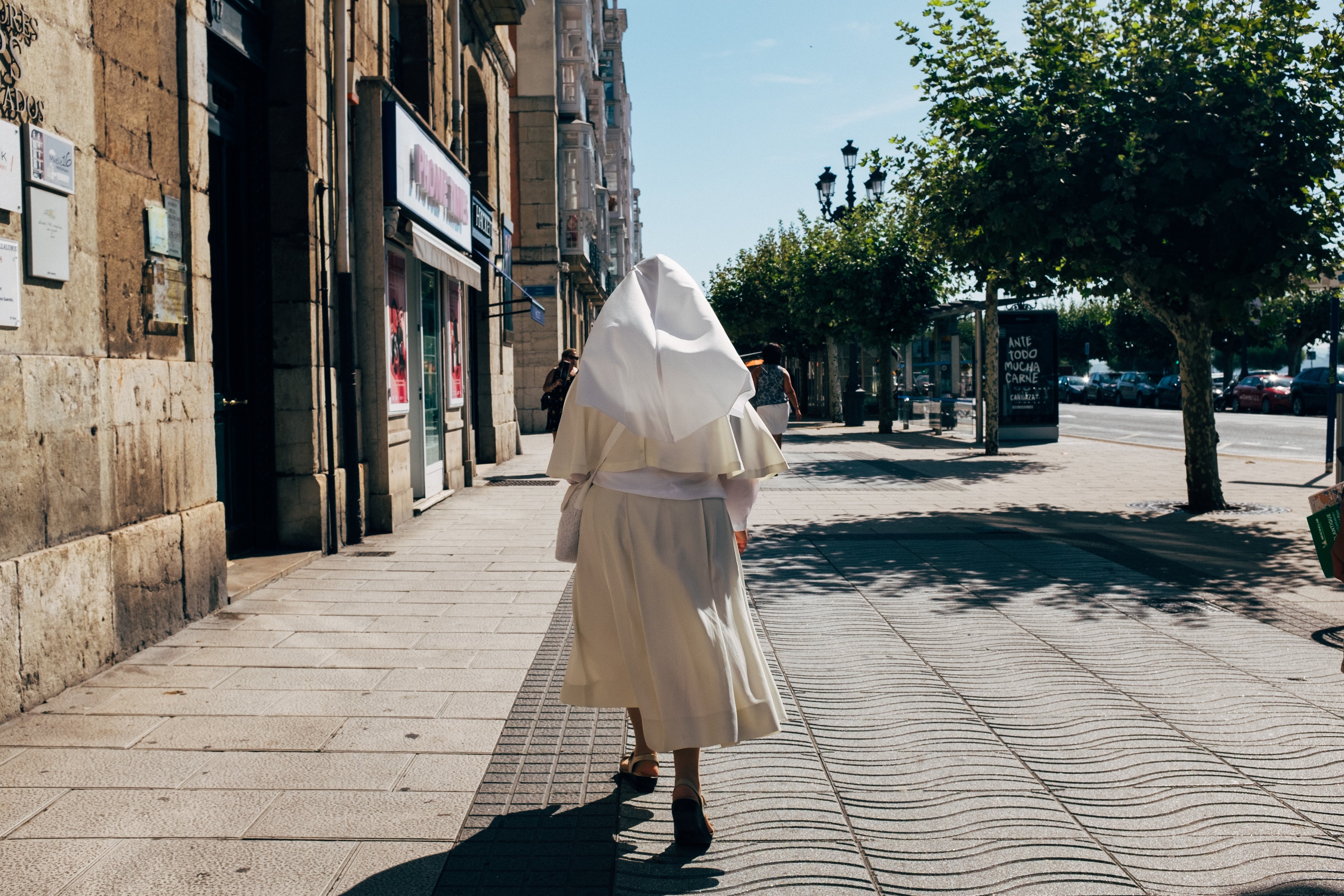 Uma freira em um hábito branco passeia em uma caminhada ensolarada de pedestre Foto 