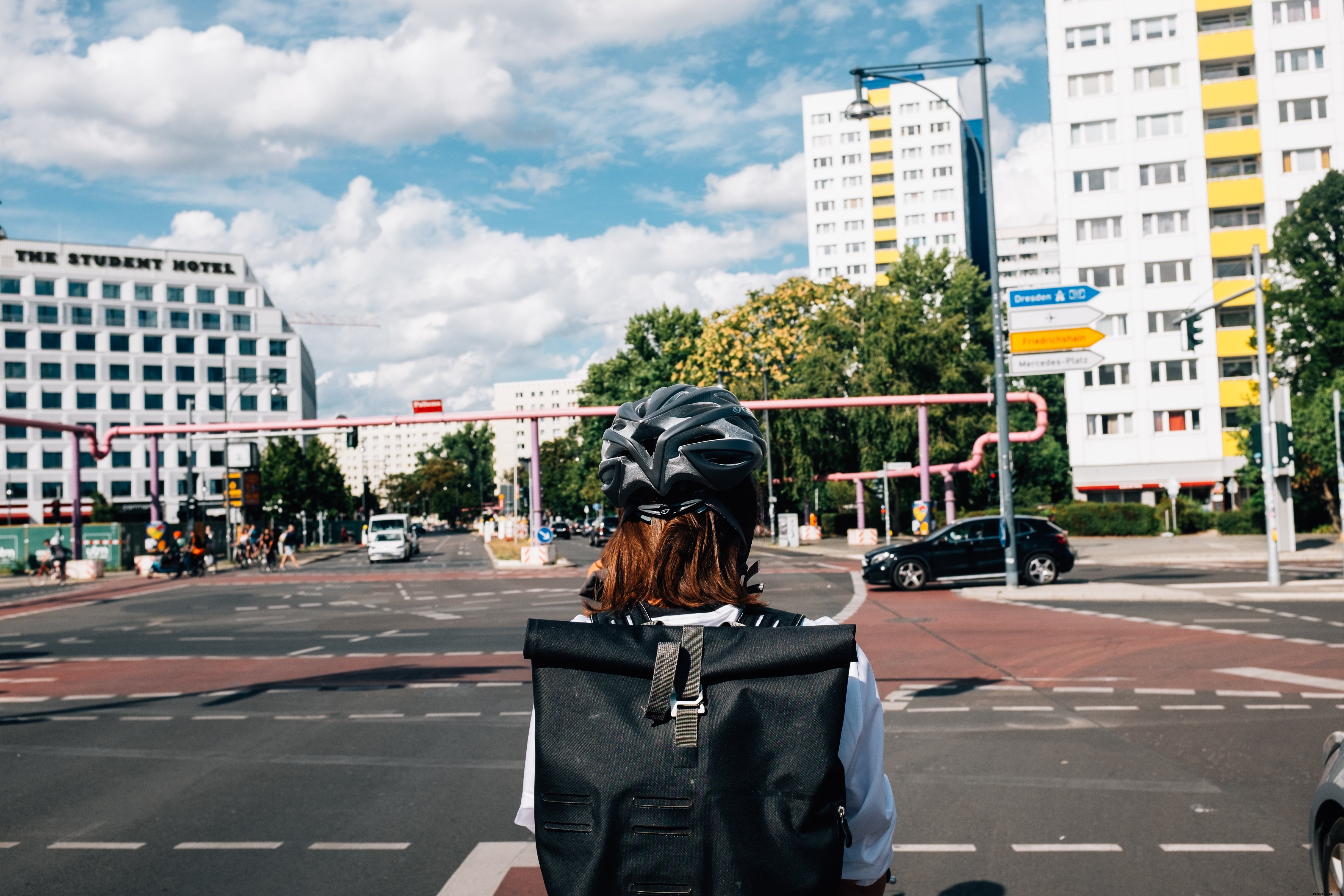 黒いヘルメットをかぶった人が街の交差点で順番を待つ写真 