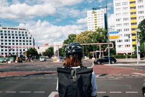 黒いヘルメットをかぶった人が街の交差点で順番を待つ写真 