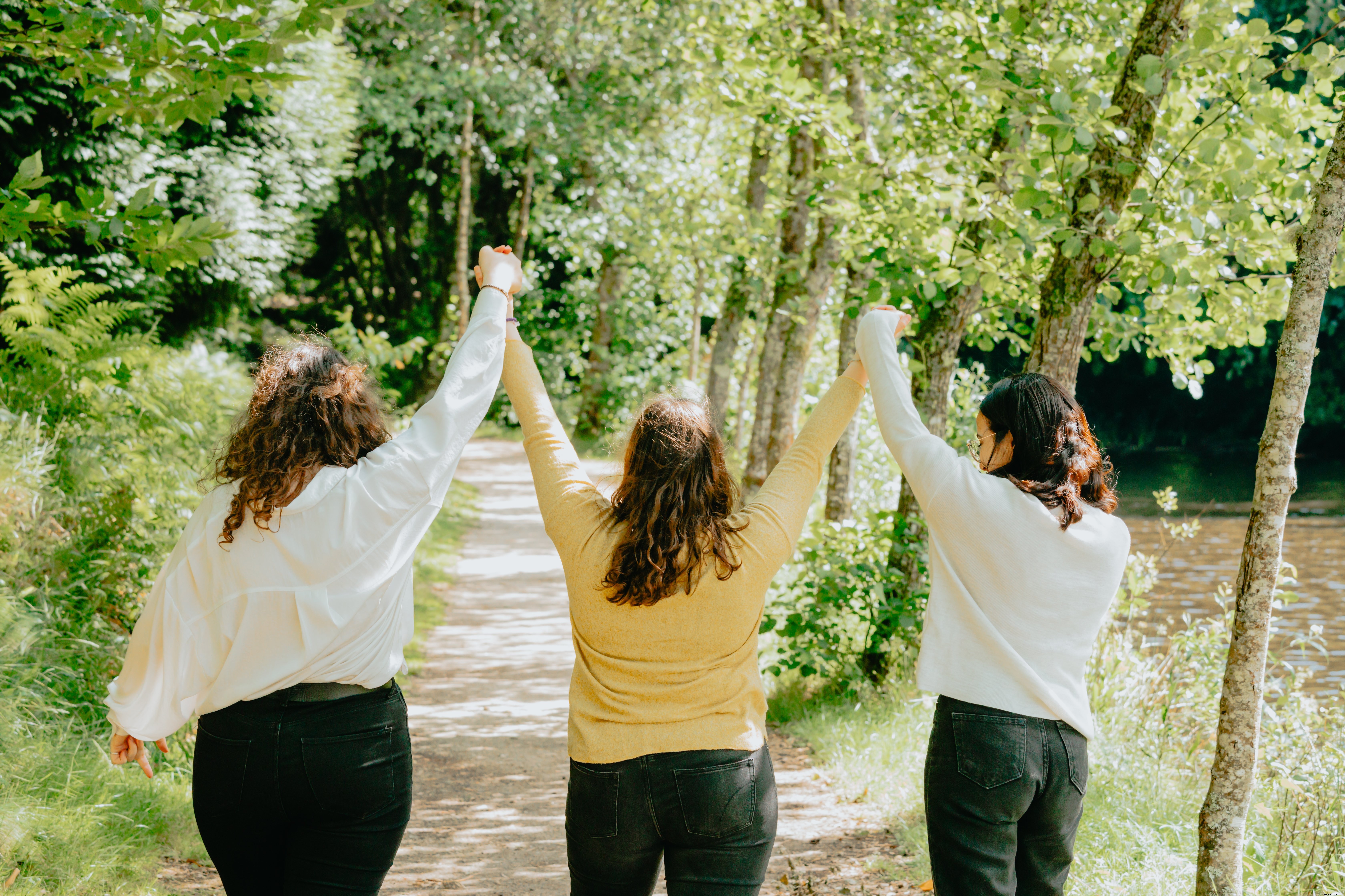 Três pessoas com as mãos ao alto em uma trilha na floresta. 