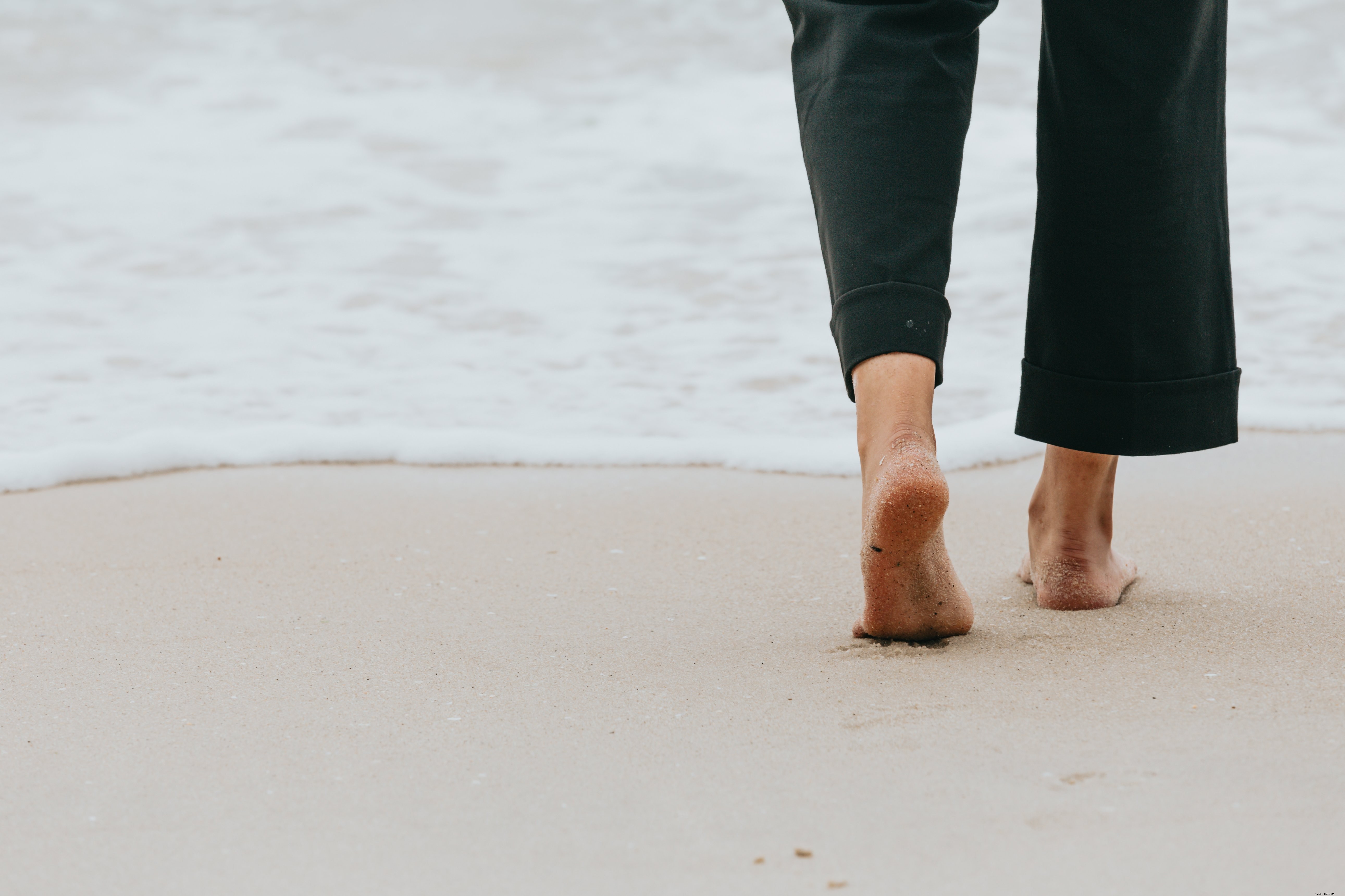 Pernas de pessoas caminhando em direção à água em uma foto de praia 