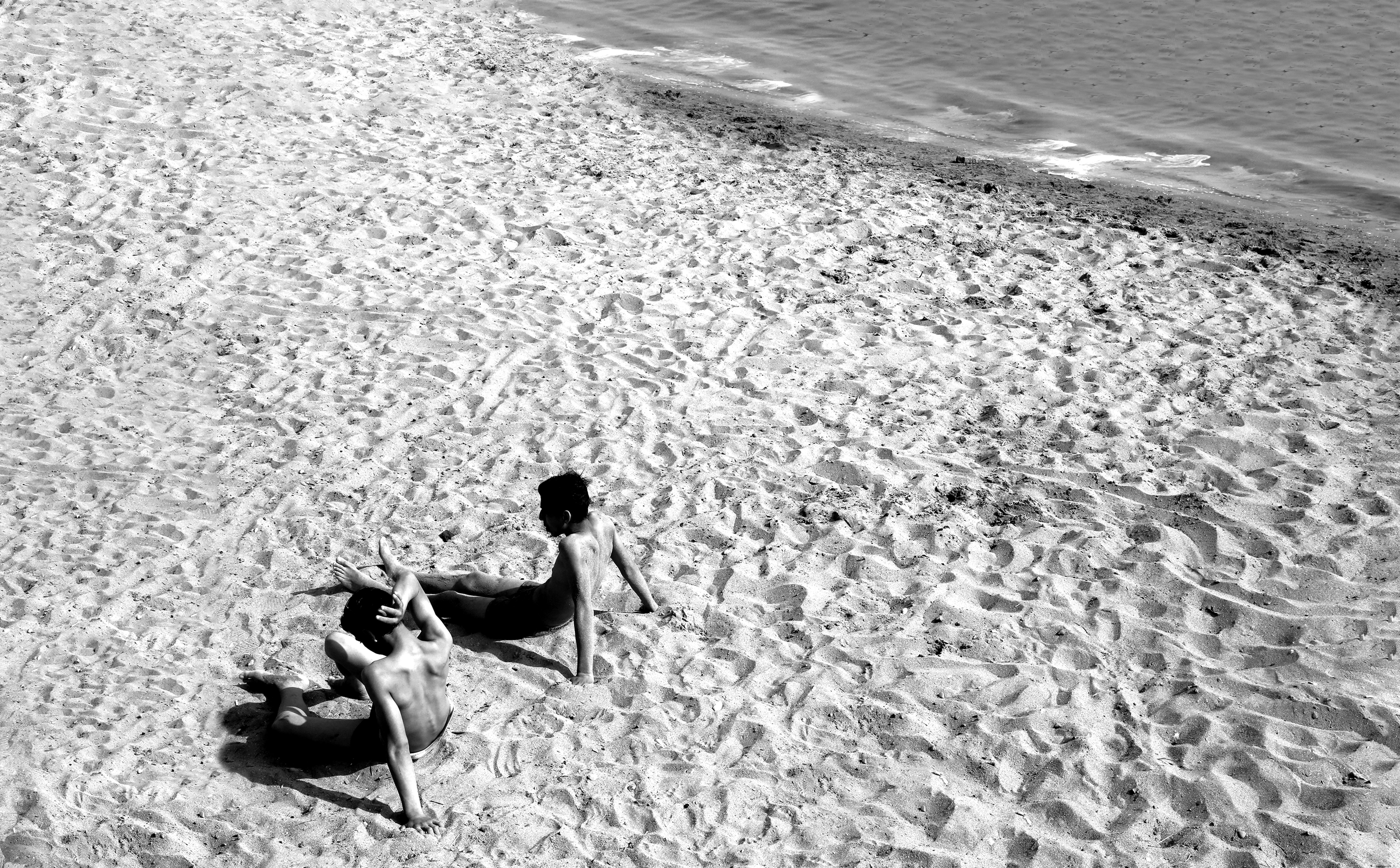 Dos personas recostadas en una playa de arena en fotografía en blanco y negro 