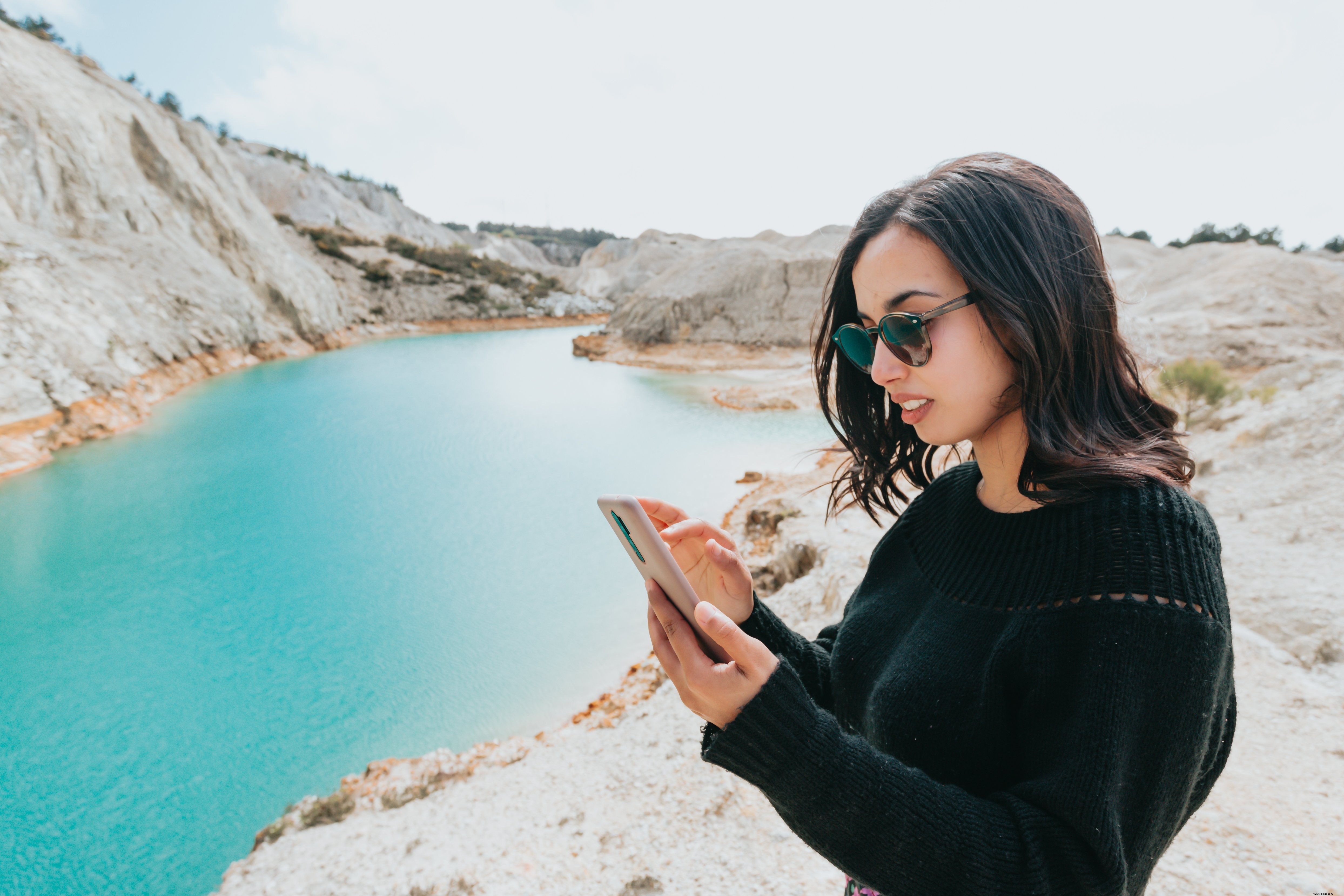 La donna guarda il suo cellulare mentre è vicino all acqua blu Foto 