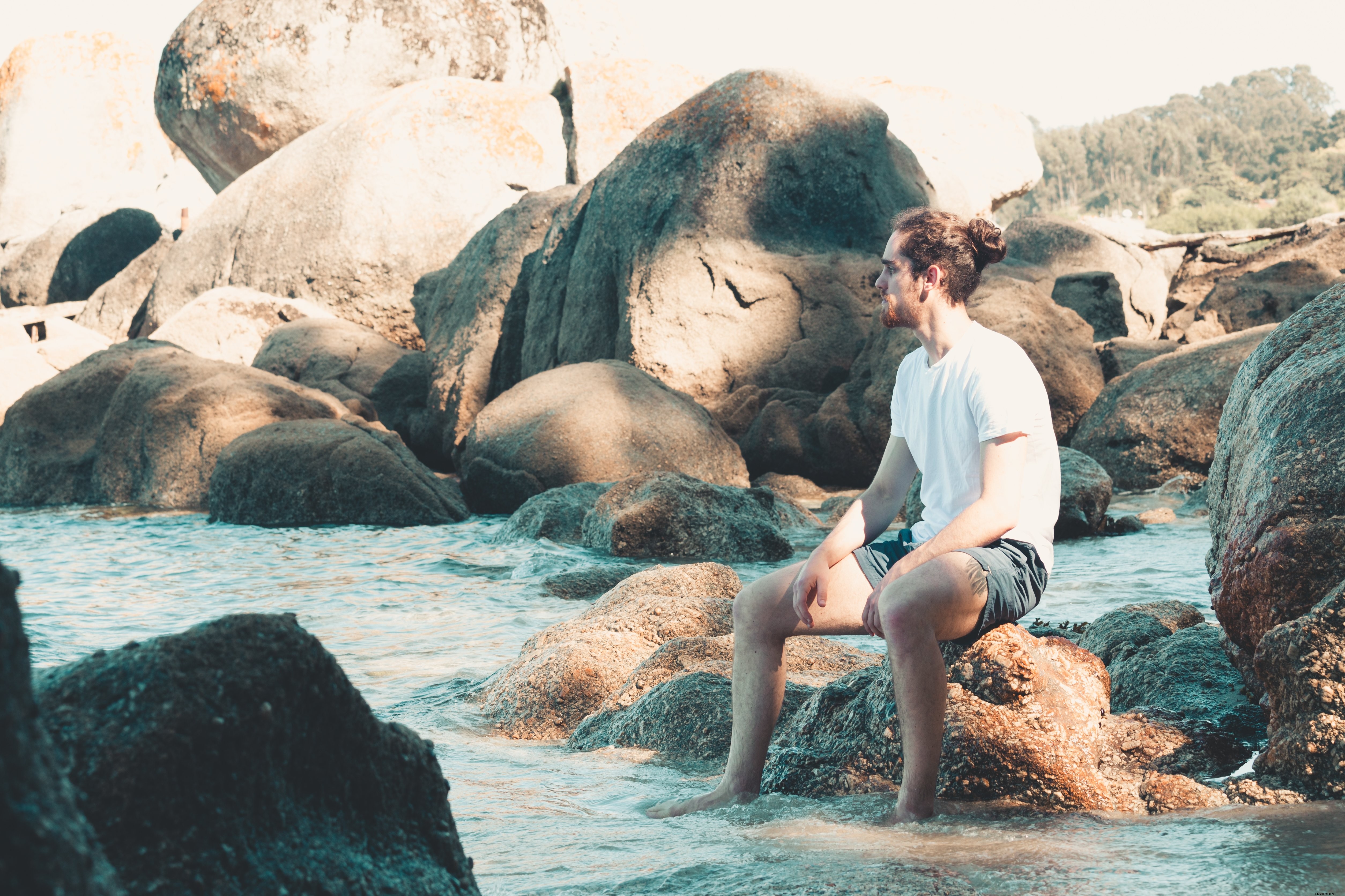 Un uomo seduto su una roccia con i piedi immersi nell acqua Foto 