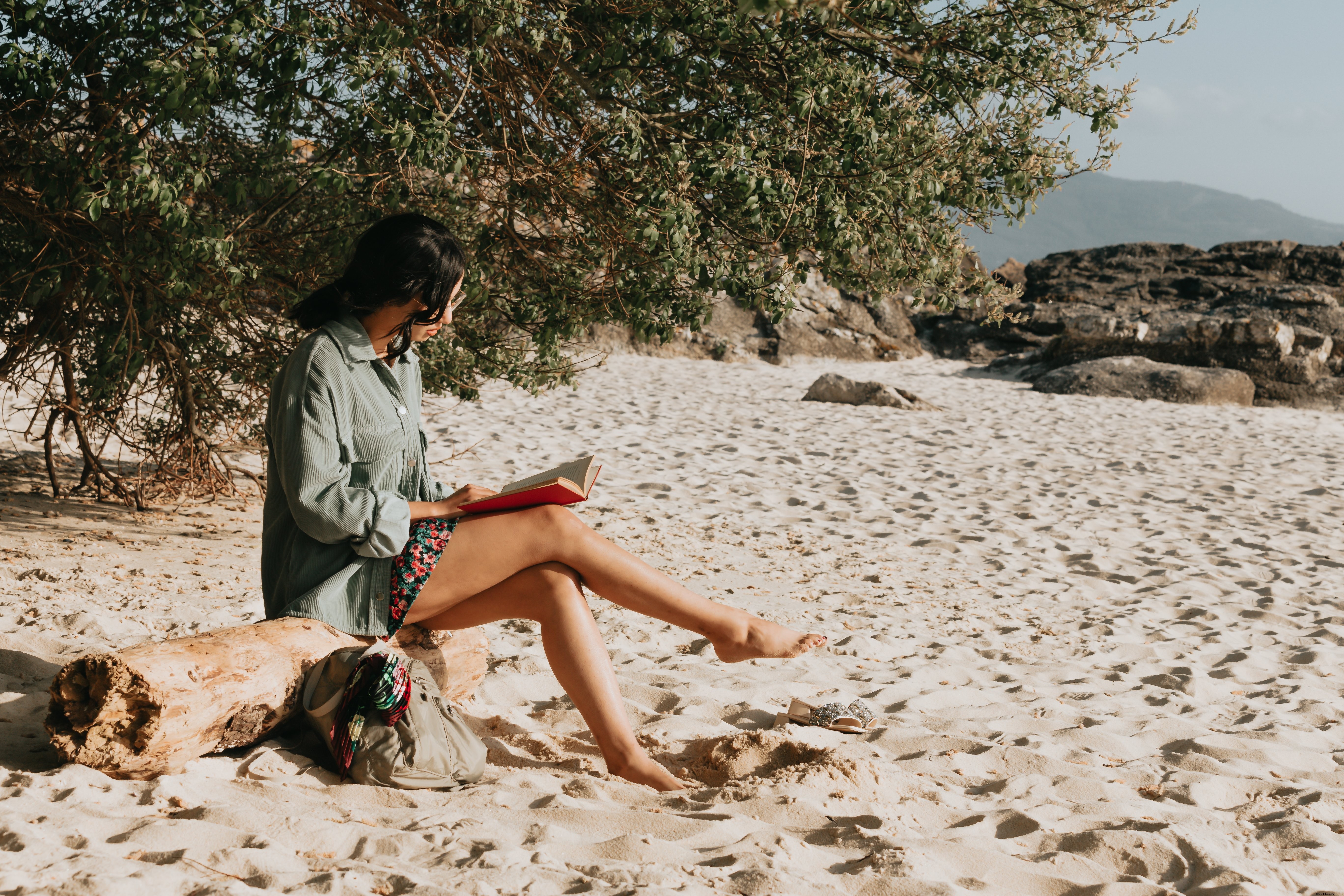 Uma pessoa lê seu romance sentada em uma foto de uma praia de areia 