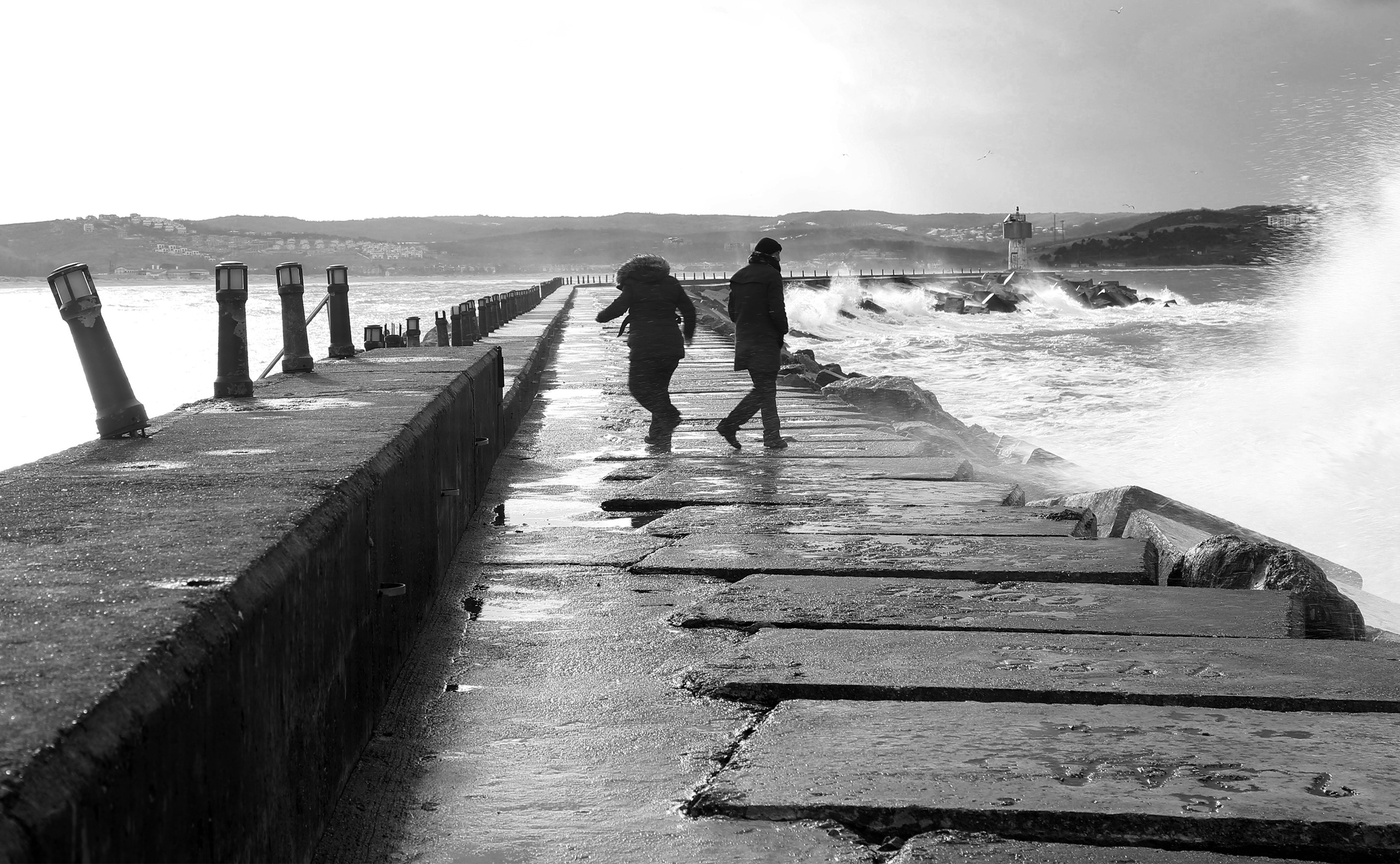 Dos personas caminando por la marea agitada del océano en foto monocroma 