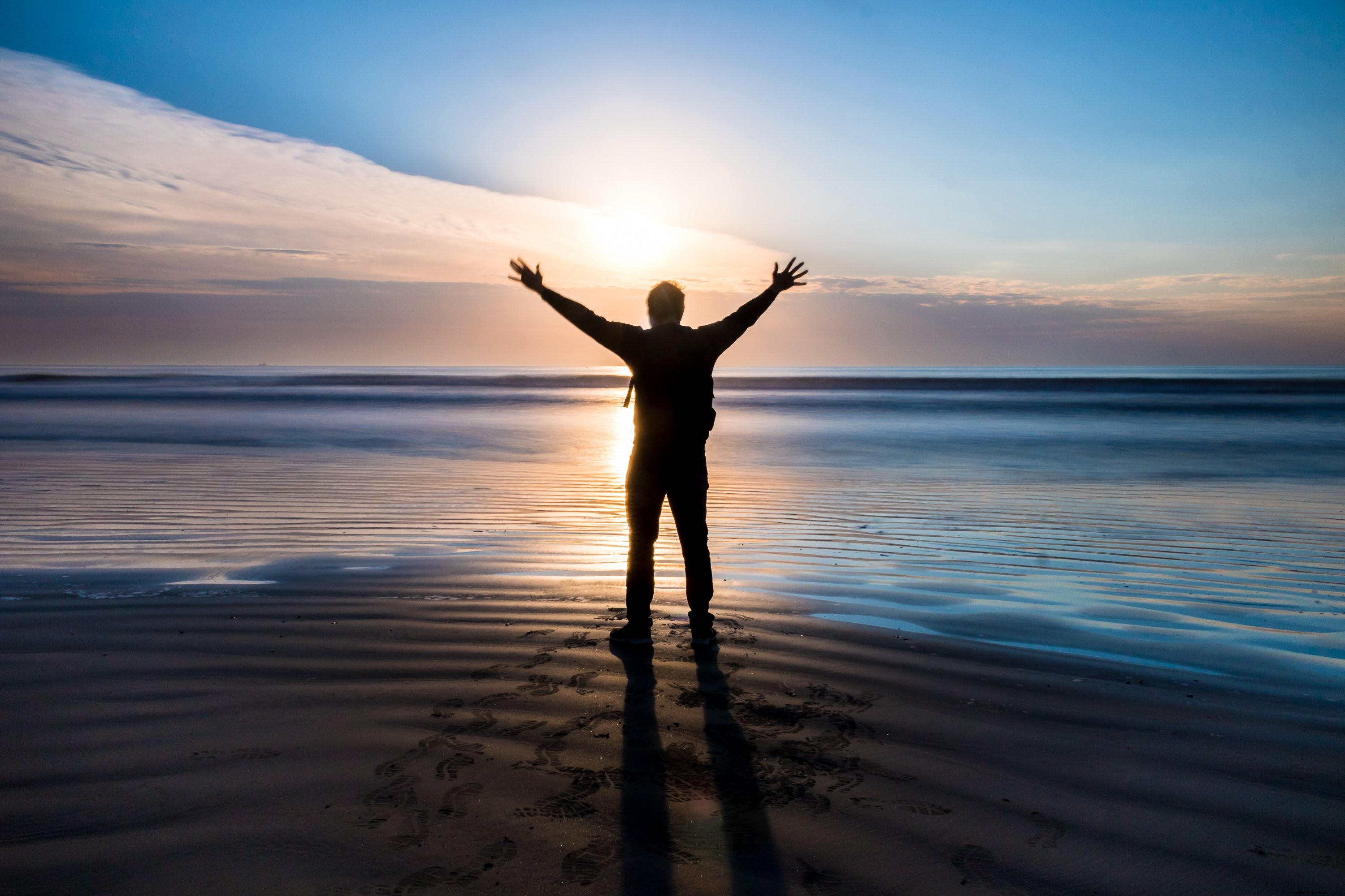 Personne se tient sur une plage avec leurs bras au coucher du soleil Photo 