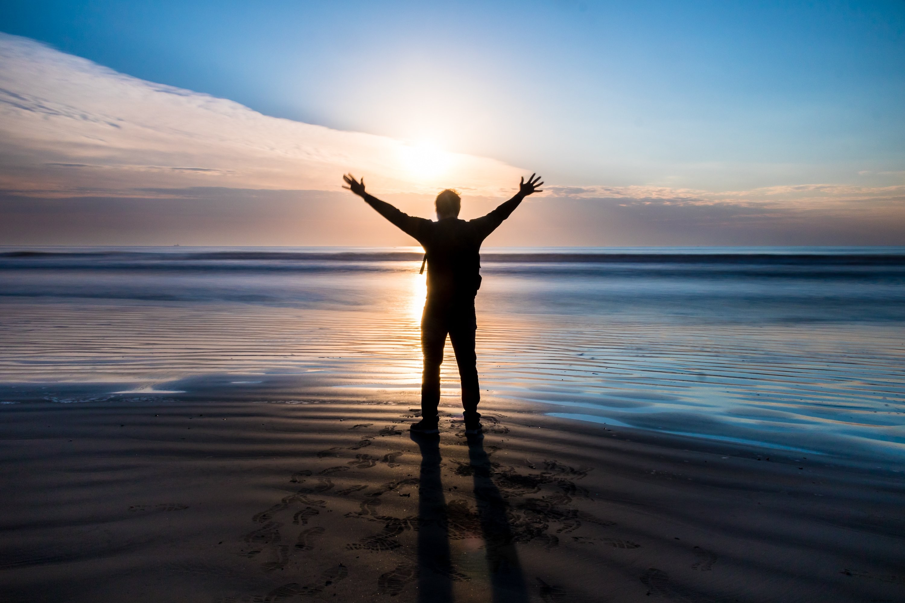 Persona de pie en una playa con los brazos extendidos al atardecer Foto 