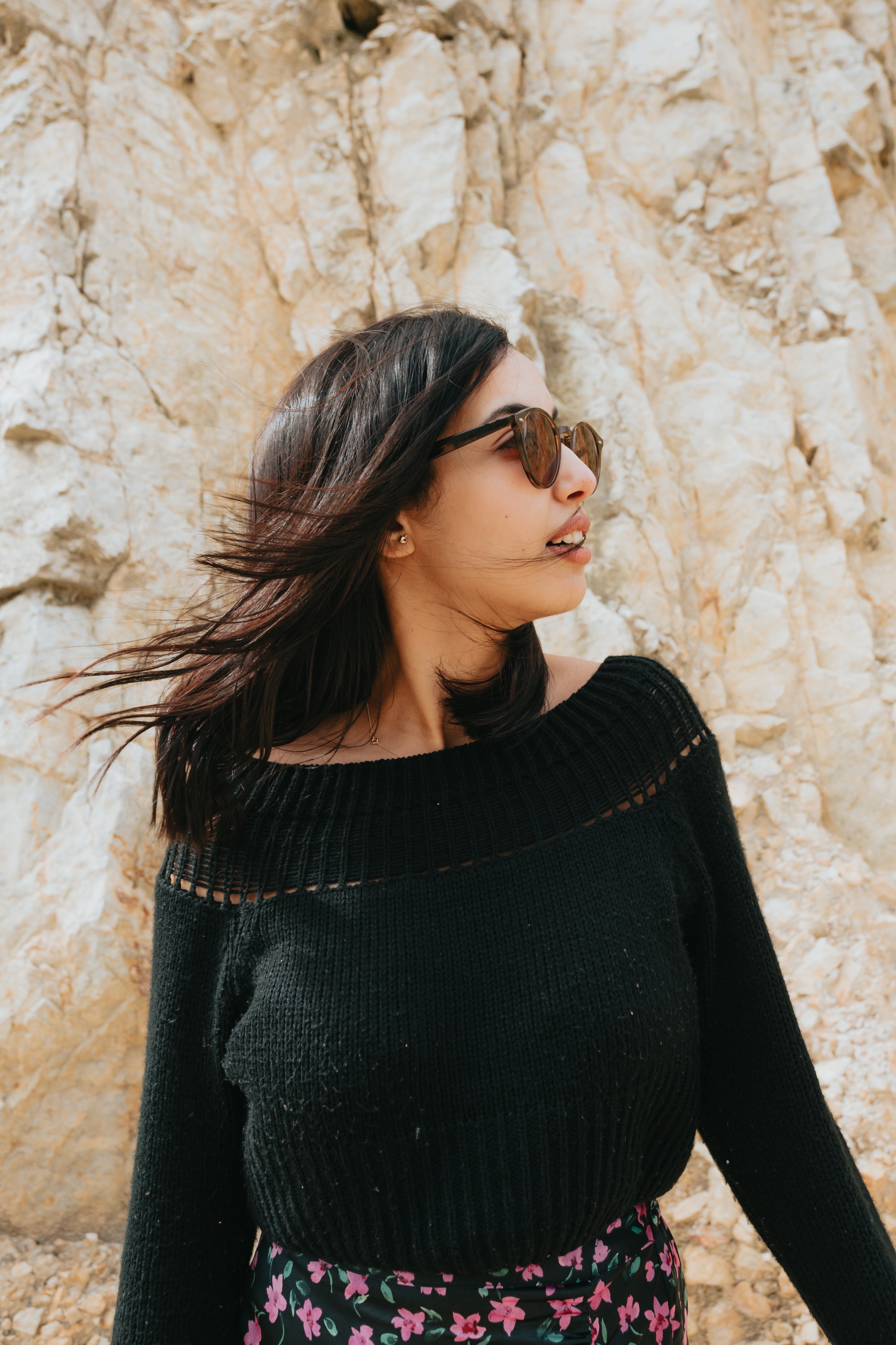 Femme portant des lunettes de soleil se tient devant une photo de surface rocheuse 