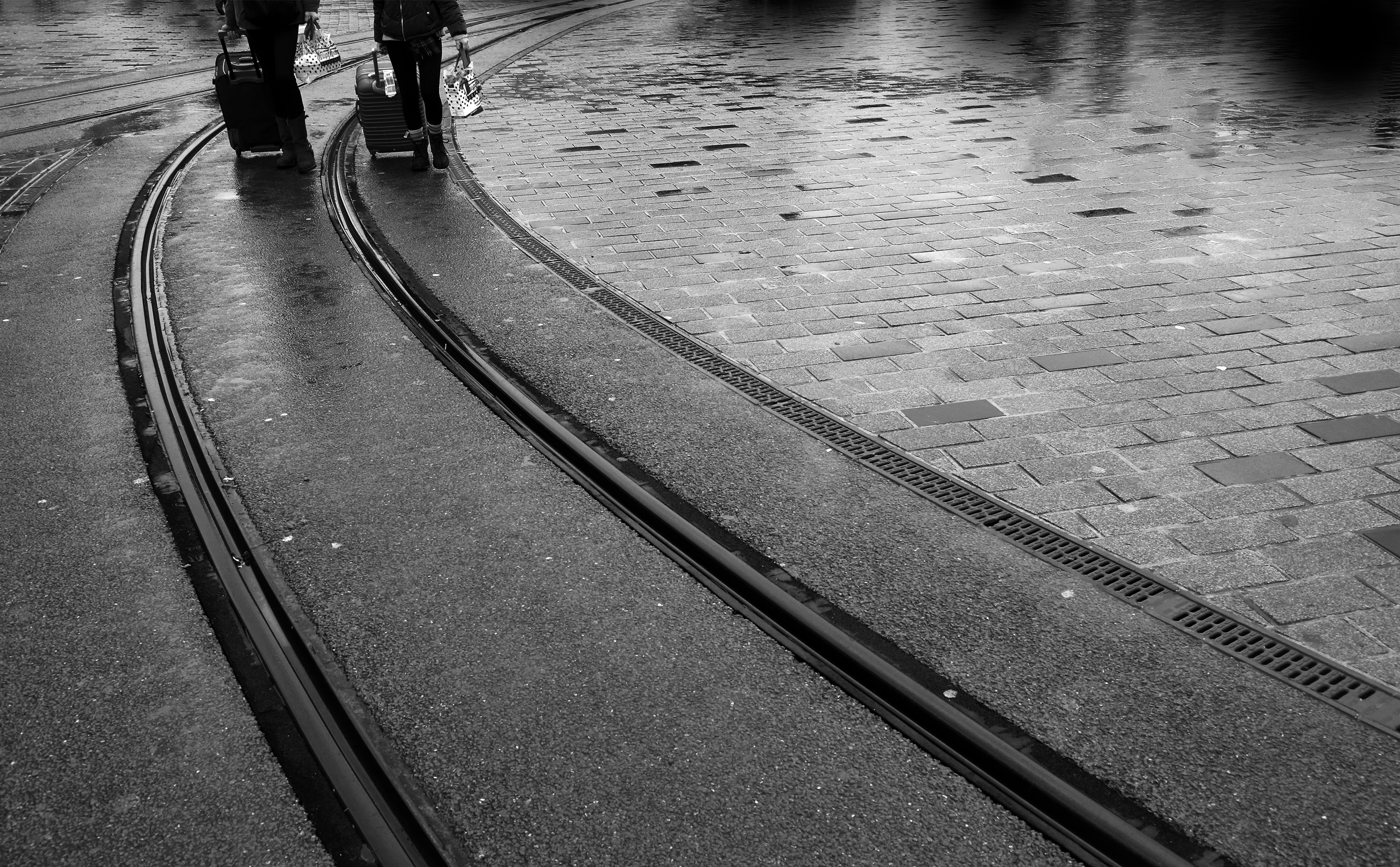 Foto em preto e branco de linhas de trem e duas pernas de pessoas 