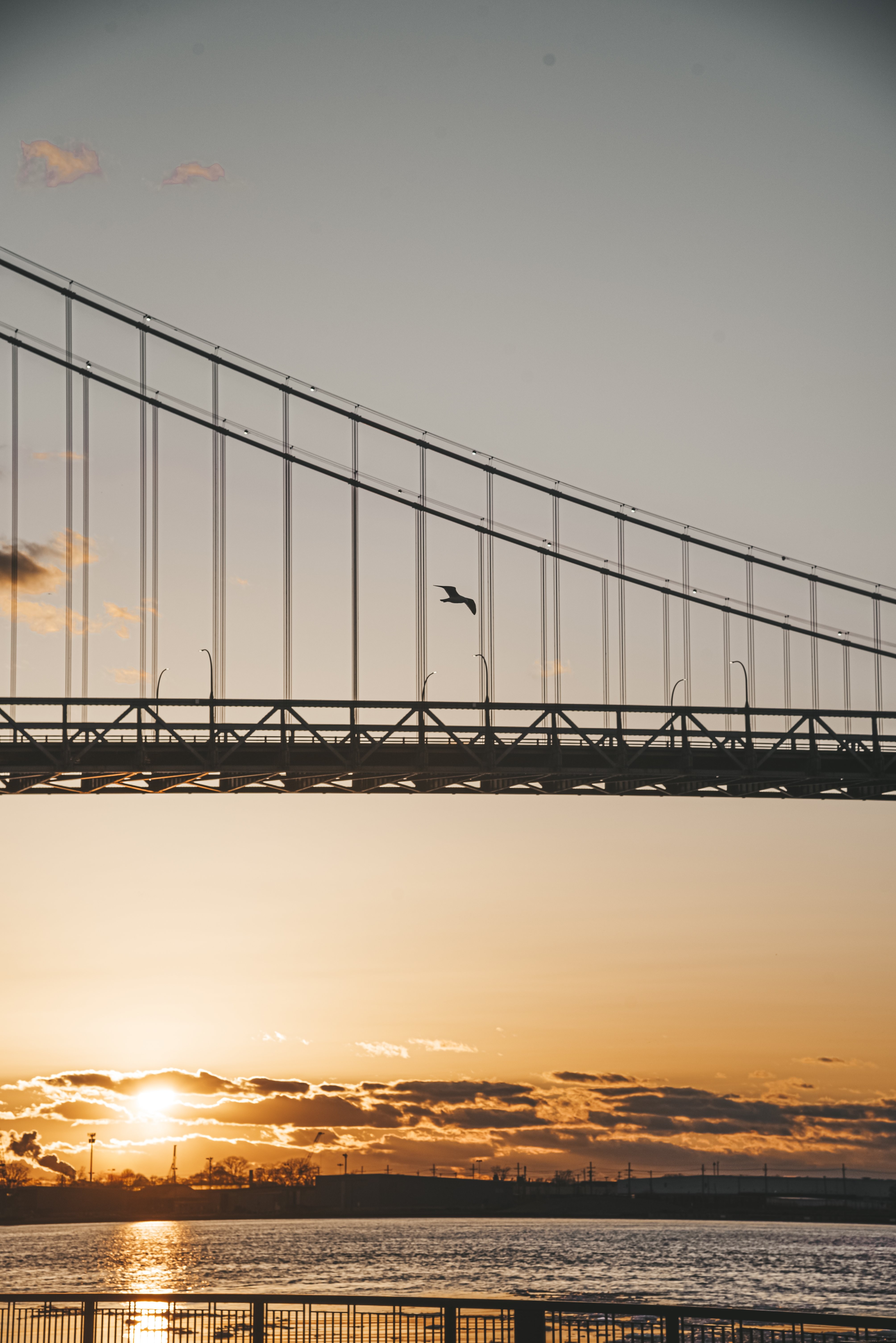 Céu laranja e amarelo sobre a água e parte da foto de uma ponte 