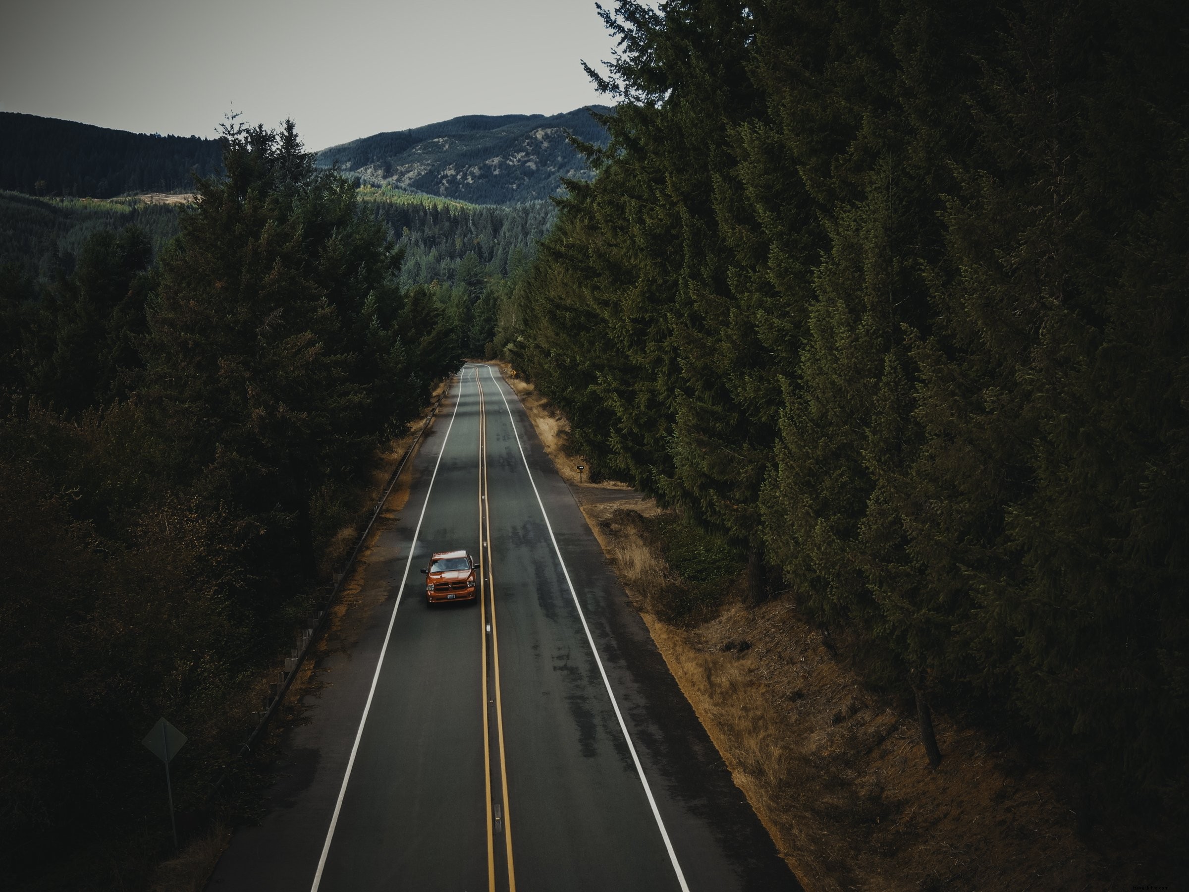 オレンジ色の車が舗装された田舎道をドライブする写真 