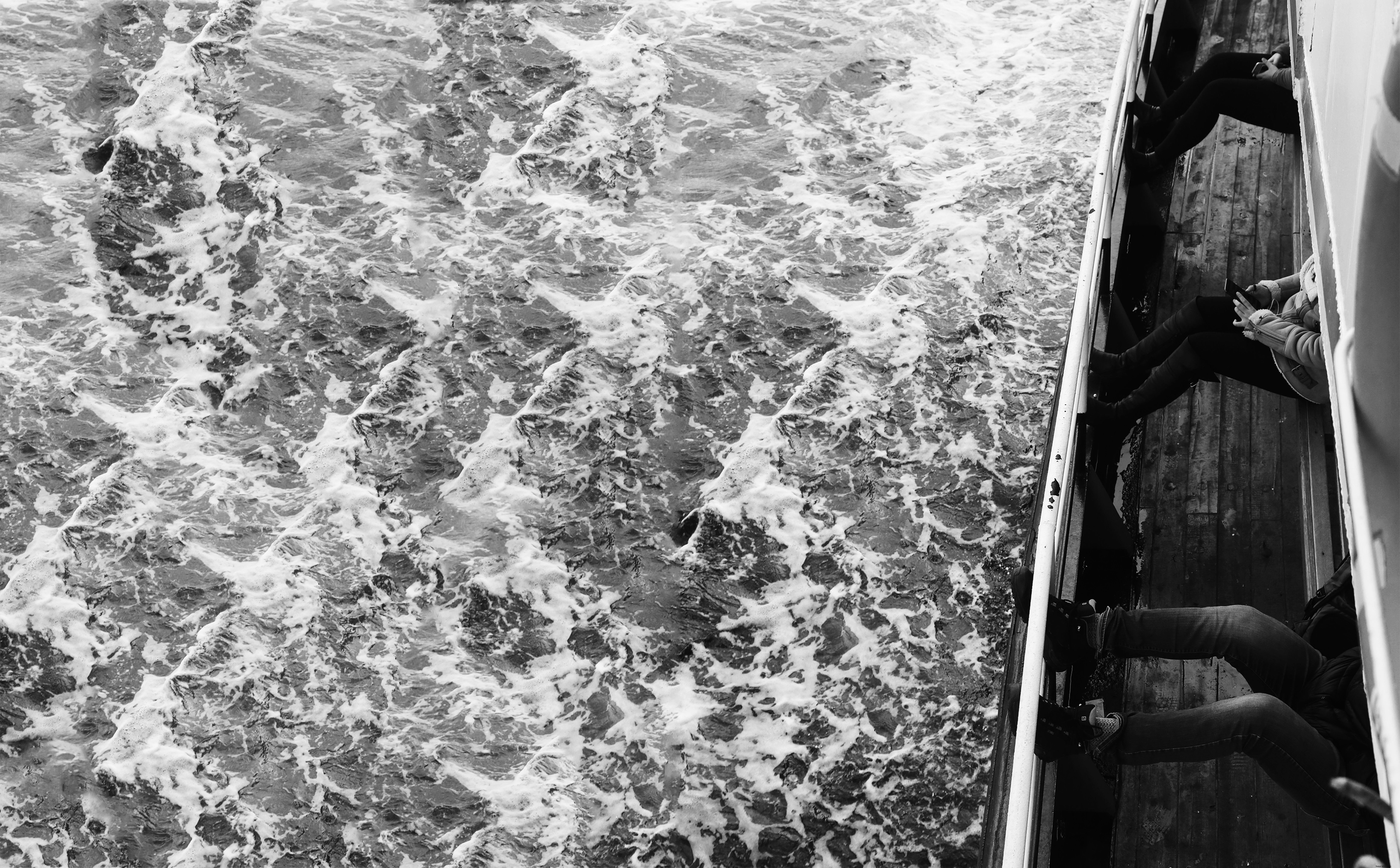 Foto em preto e branco de ondas e pessoas em um barco. 