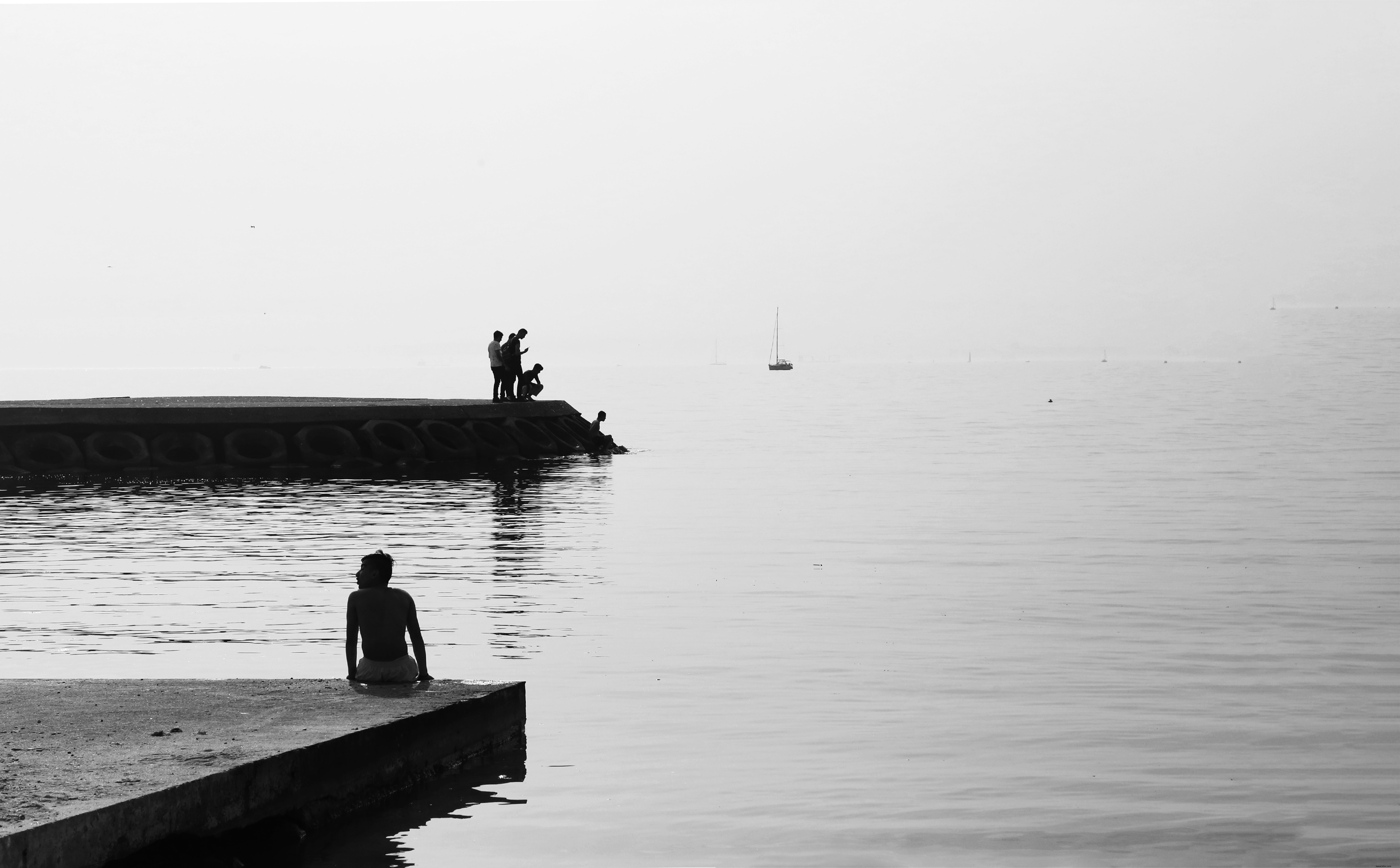 Fotografía en blanco y negro de personas en una orilla de cemento por fotografía de agua inmóvil 