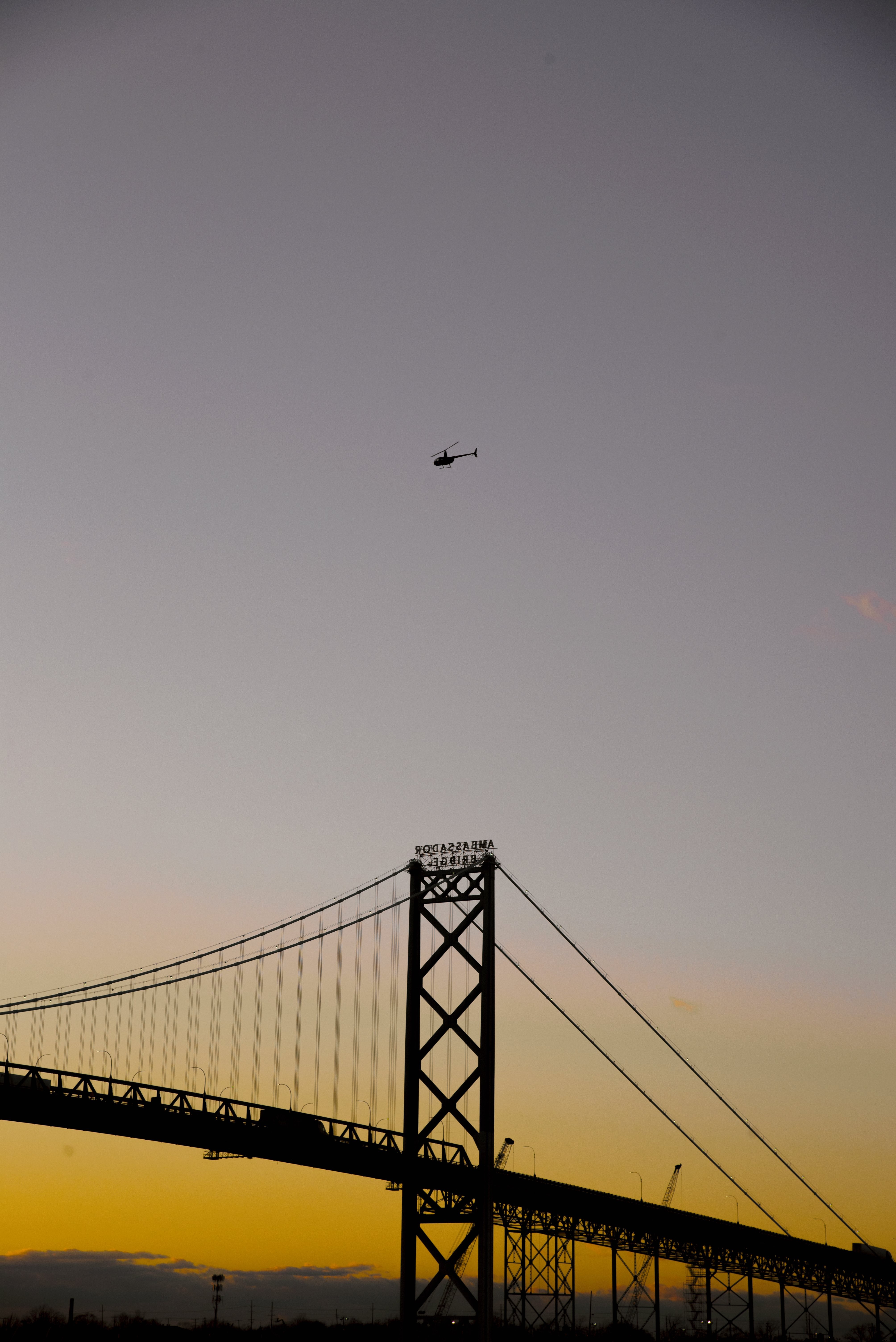 シルエットの大きな橋と日没時のヘリコプター写真 