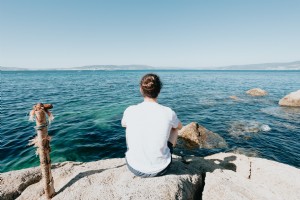 Persona sentada sobre una roca y mira hacia el agua Foto 
