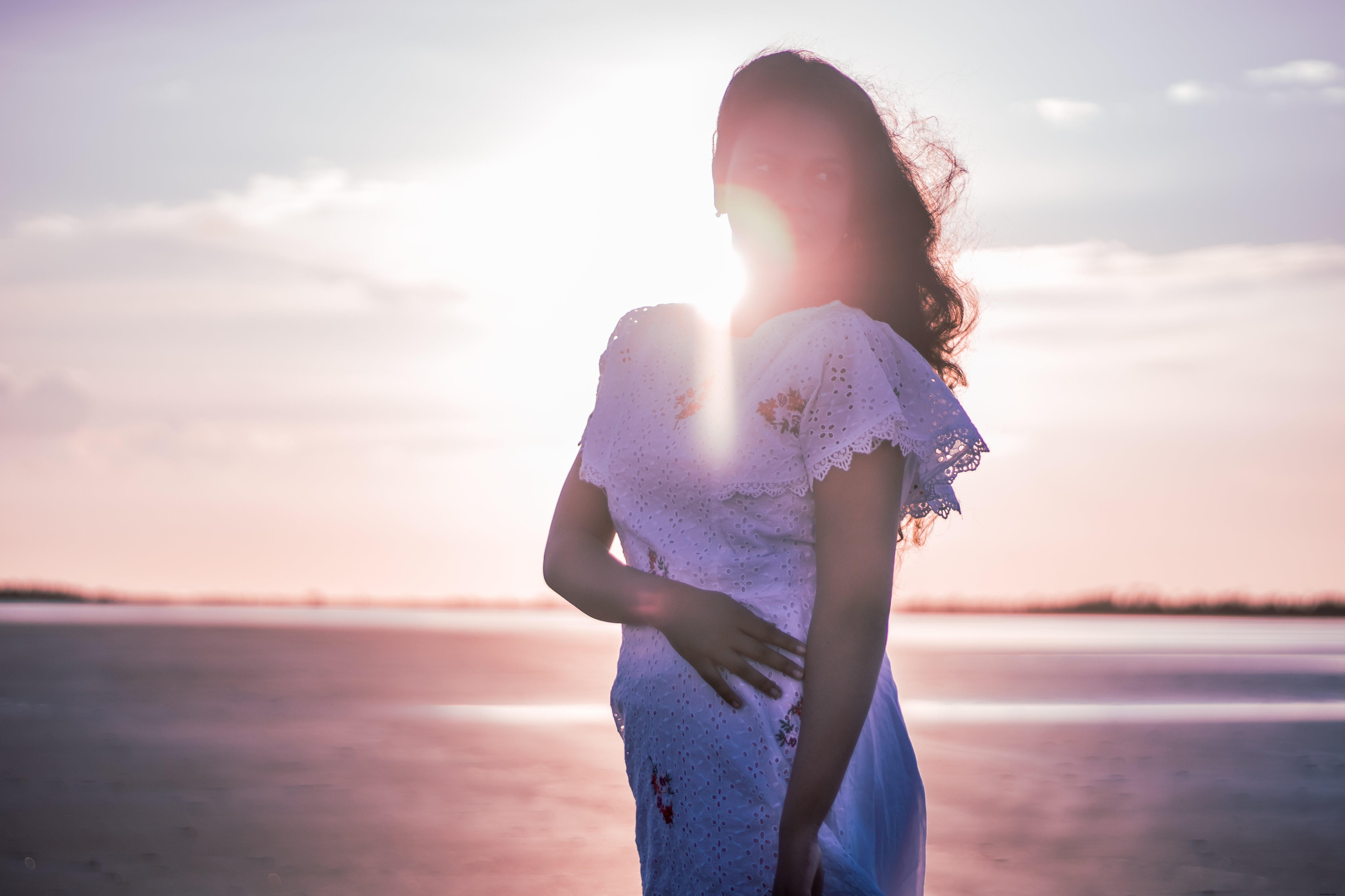 白いドレスを着た人が日没の写真でビーチに立つ 