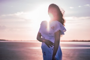 Personne dans une robe blanche se dresse sur la plage au coucher du soleil Photo 